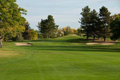 Golf course fairway leading to a green with sand bunkers and trees under a clear sky.