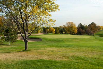Golf course fairway with sand bunkers, trees with autumn foliage, and a clear sky.