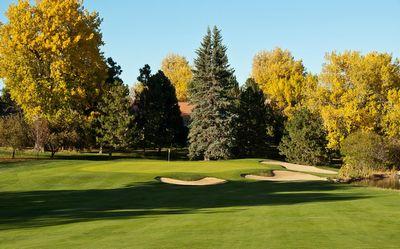 Golf course green with sand bunkers and trees with yellow autumn leaves under a clear blue sky.
