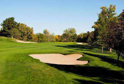 Golf course fairway with a sand bunker surrounded by green grass and trees under a clear blue sky.