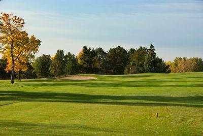 Golf course fairway with a sand bunker, surrounded by trees under a clear sky.