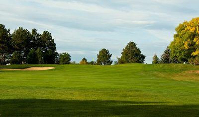Green golf course fairway with a sand bunker on the left and trees in the background under a partly cloudy sky.