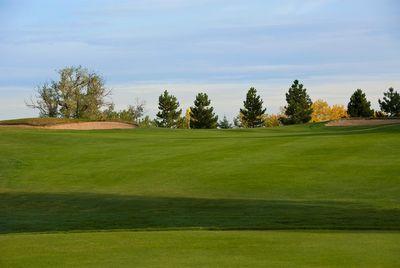 Golf course fairway with sand bunkers and trees under a cloudy sky.