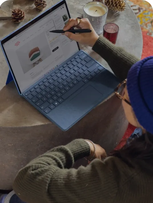 Person using a stylus to interact with a tablet keyboard on a round table with pinecones and candles.