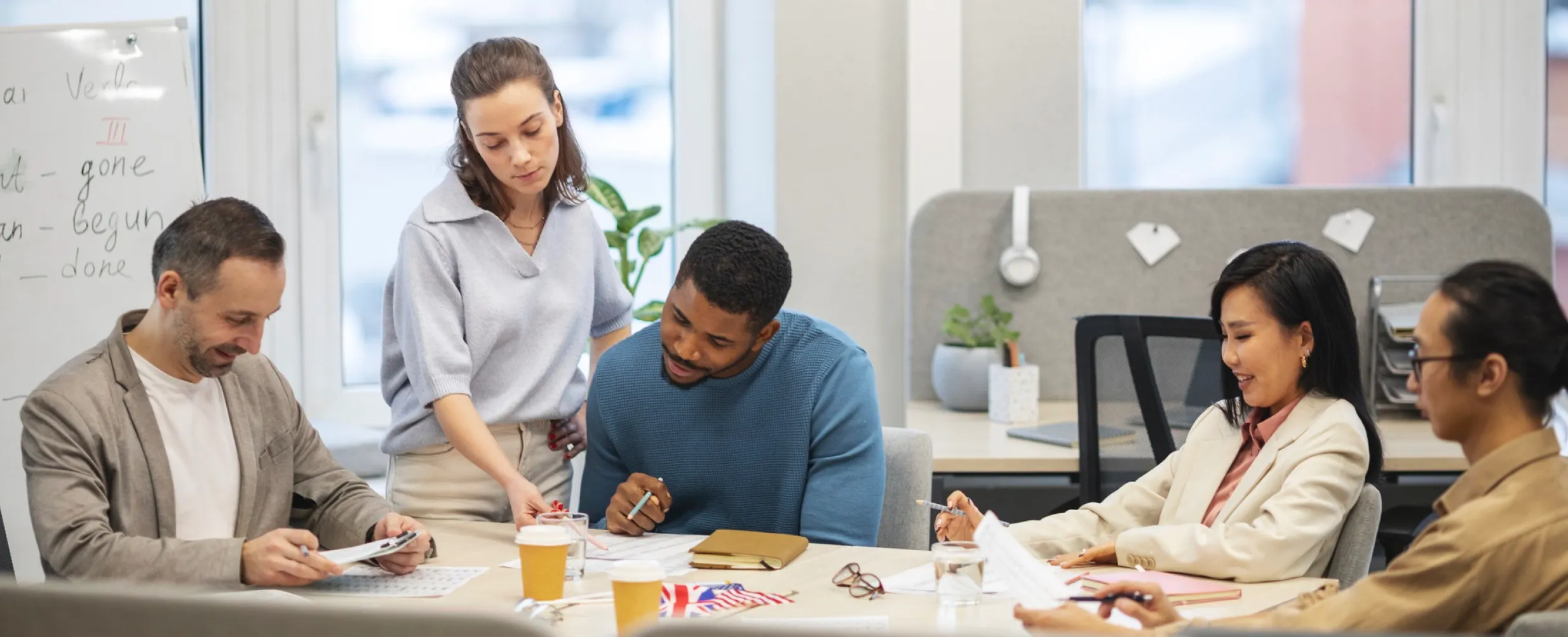 Four colleagues collaborating around a table with documents, coffee cups, and small flags in a modern office.
