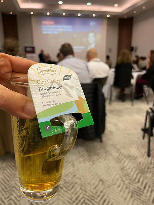 Two people sitting at a table, with one showing code on a laptop screen, in a room with snowy mountains outside the window