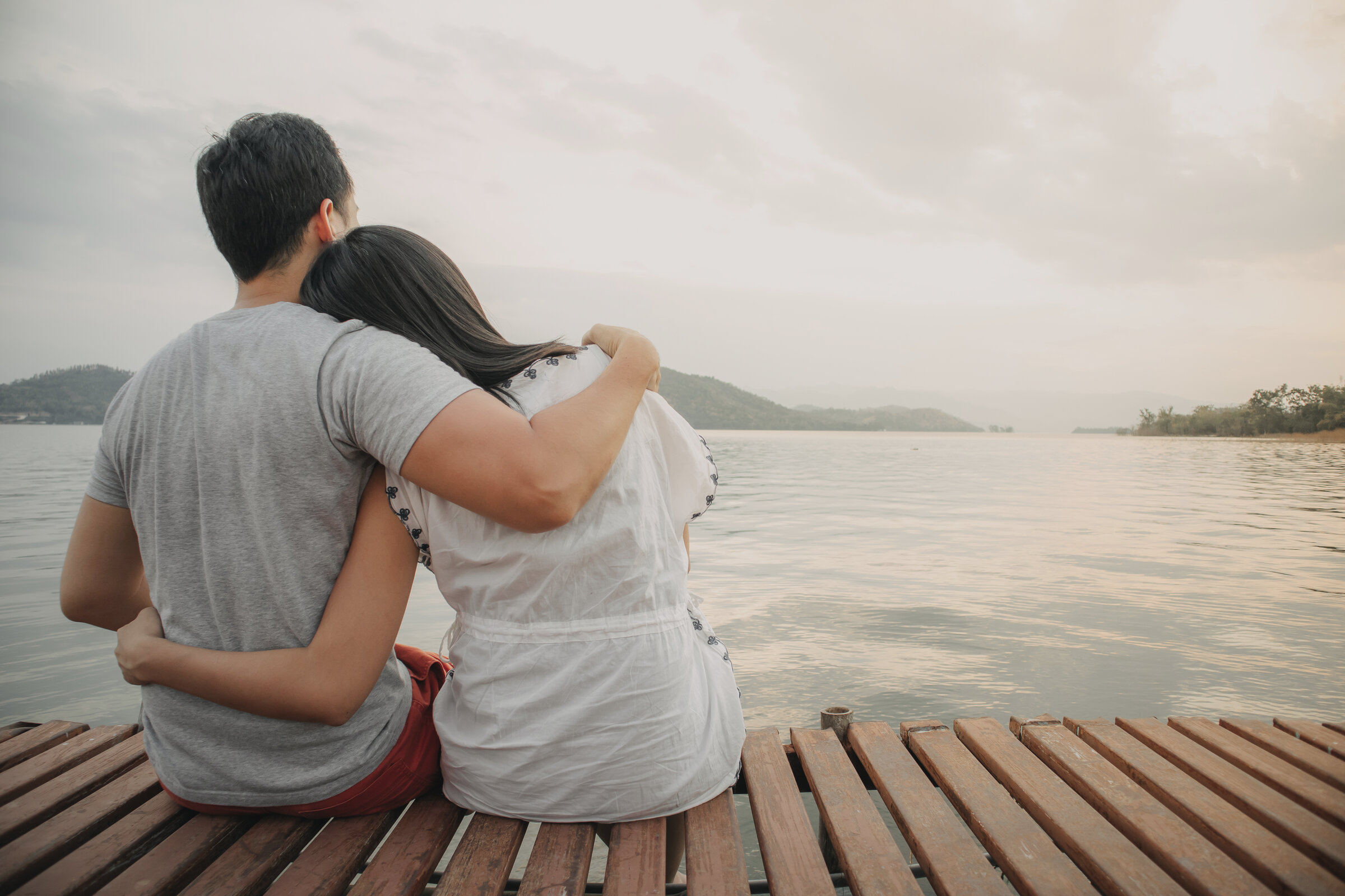 Couple embracing on a lakeside deck overlooking a serene alpine lake at dawn