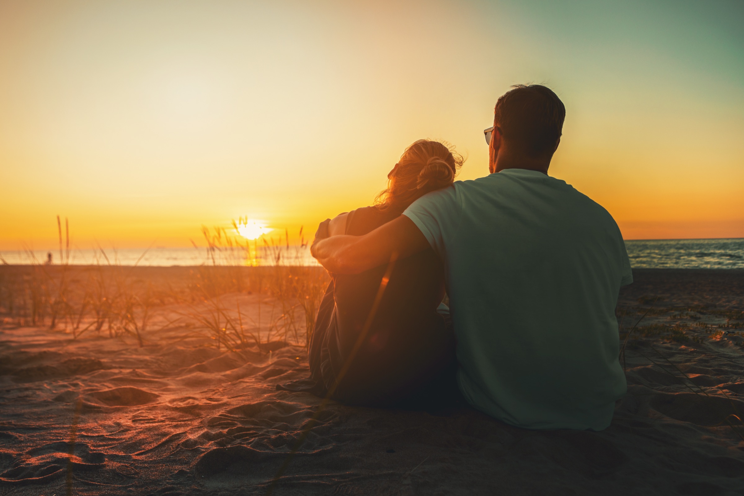 A couple sitting together on the sand at golden sunset