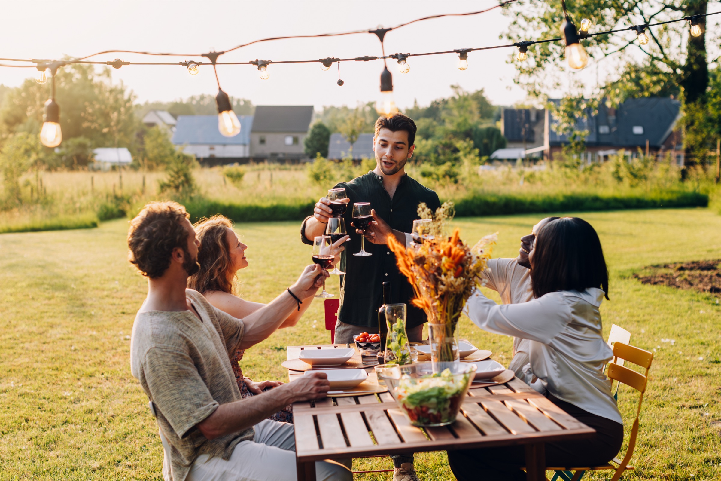 Friends toasting at an outdoor dinner under string lights