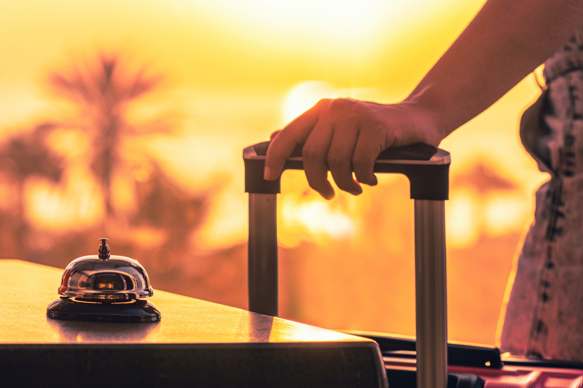 A hand resting on a suitcase beside a service bell at sunset