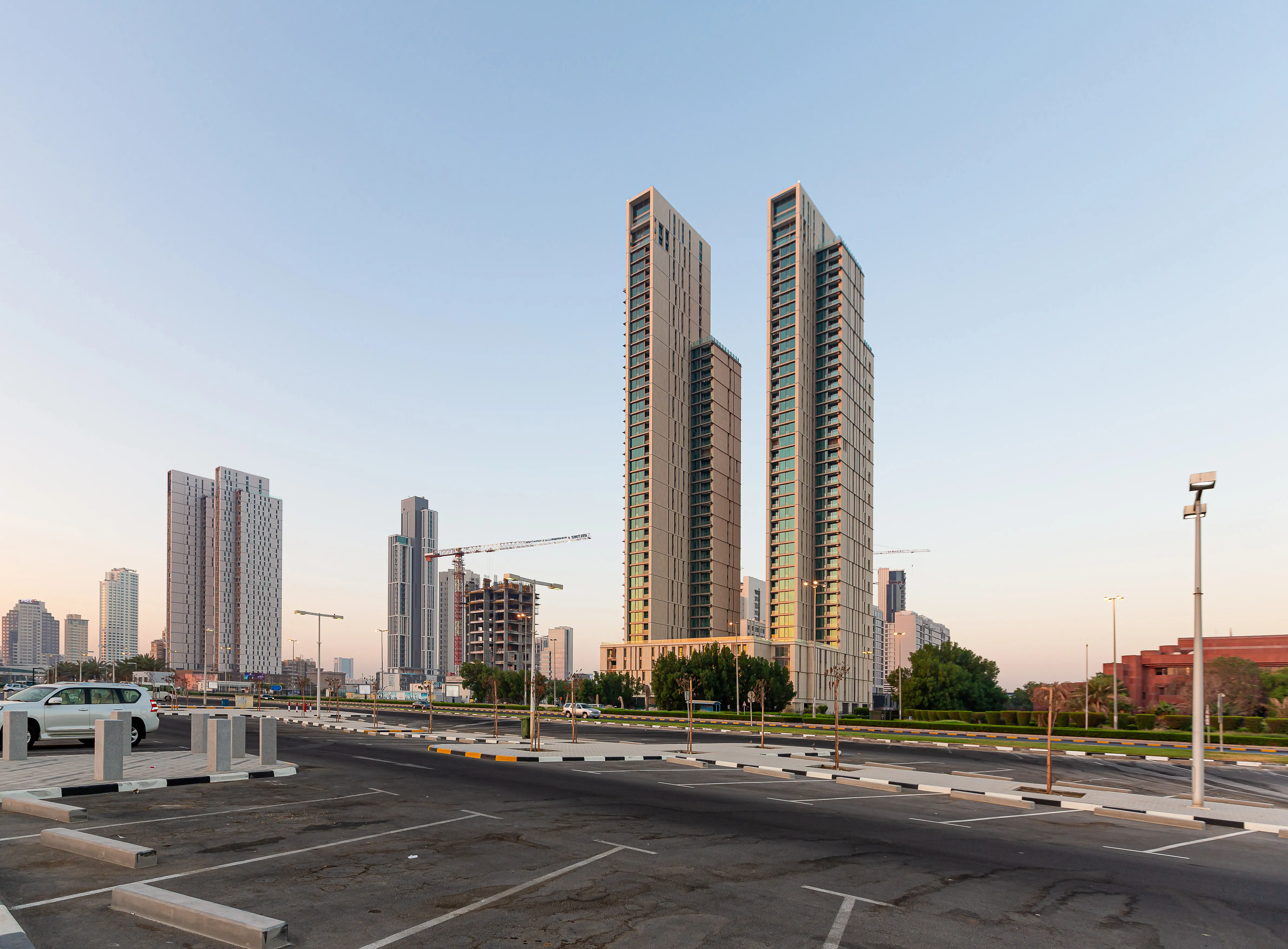 Twin residential towers of Hessah Al Mubarak rising above a podium in Kuwait City, seen from a broad street with the wider skyline behind