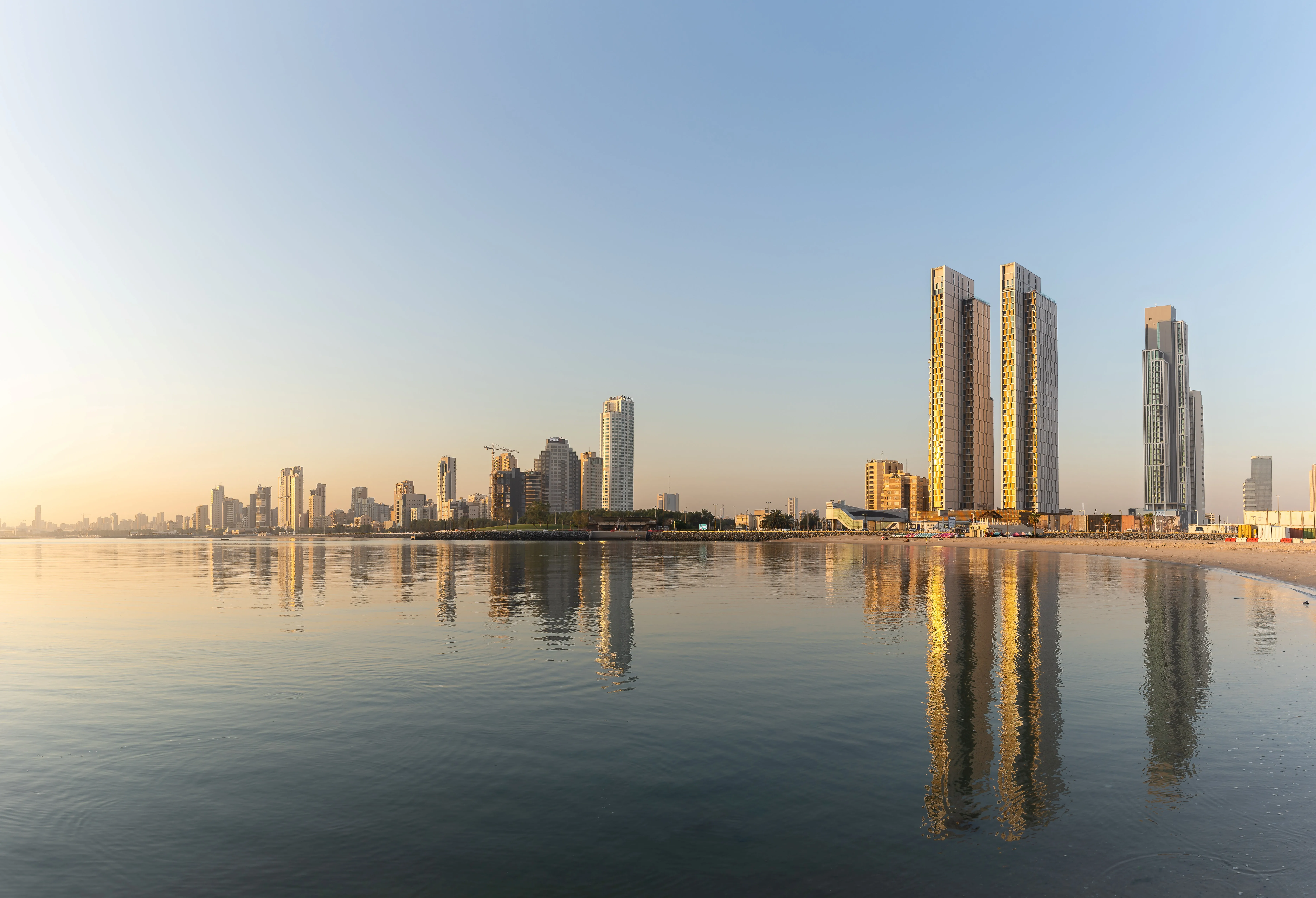 Coastal skyline of Hessah Al Mubarak in Kuwait City, twin slender towers and a podium reflected in calm sea water at dawn