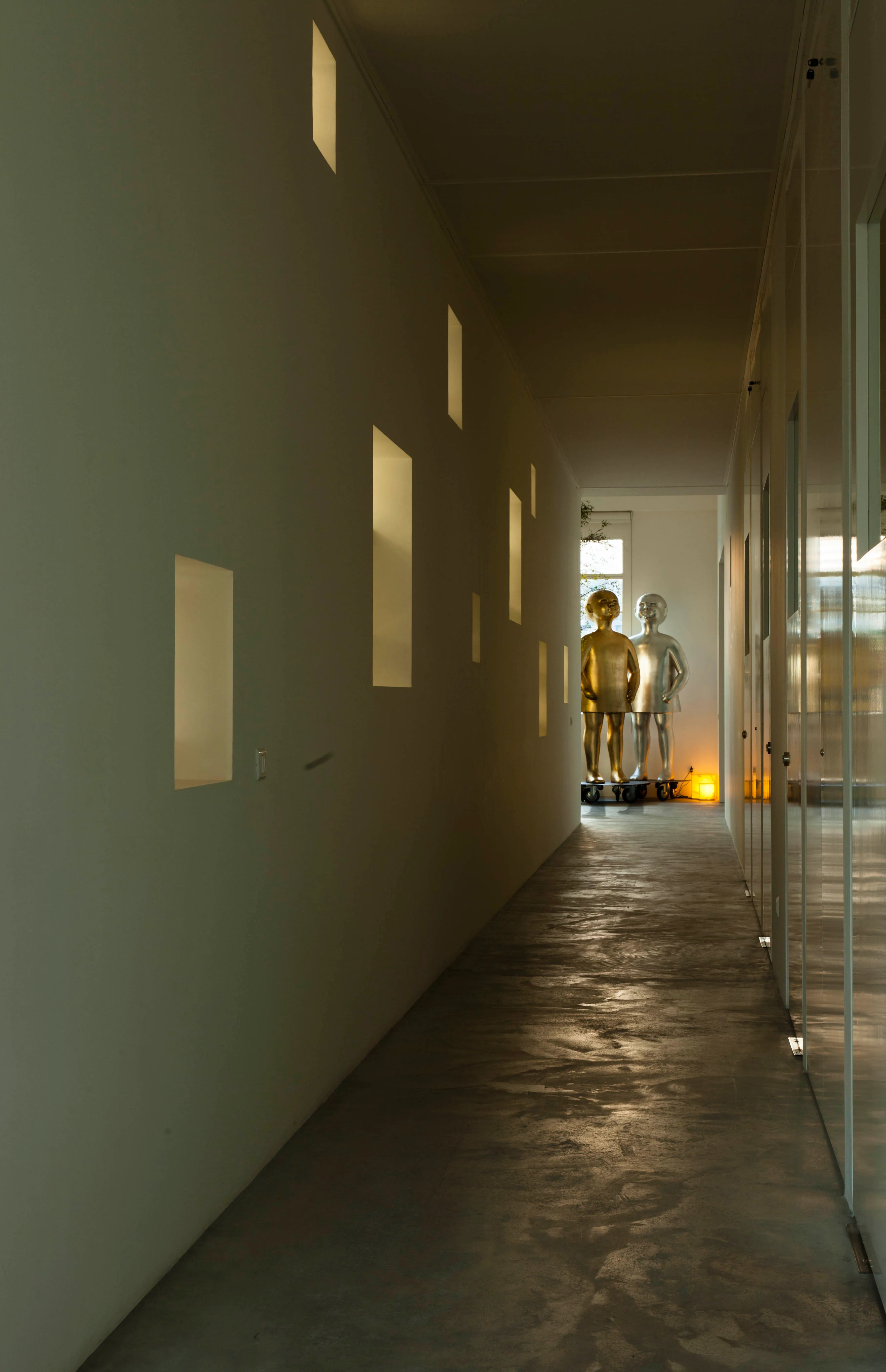 Long corridor at the ngª Office in Beirut, recessed wall niches glowing with light leading toward two life-sized metallic figurine sculptures