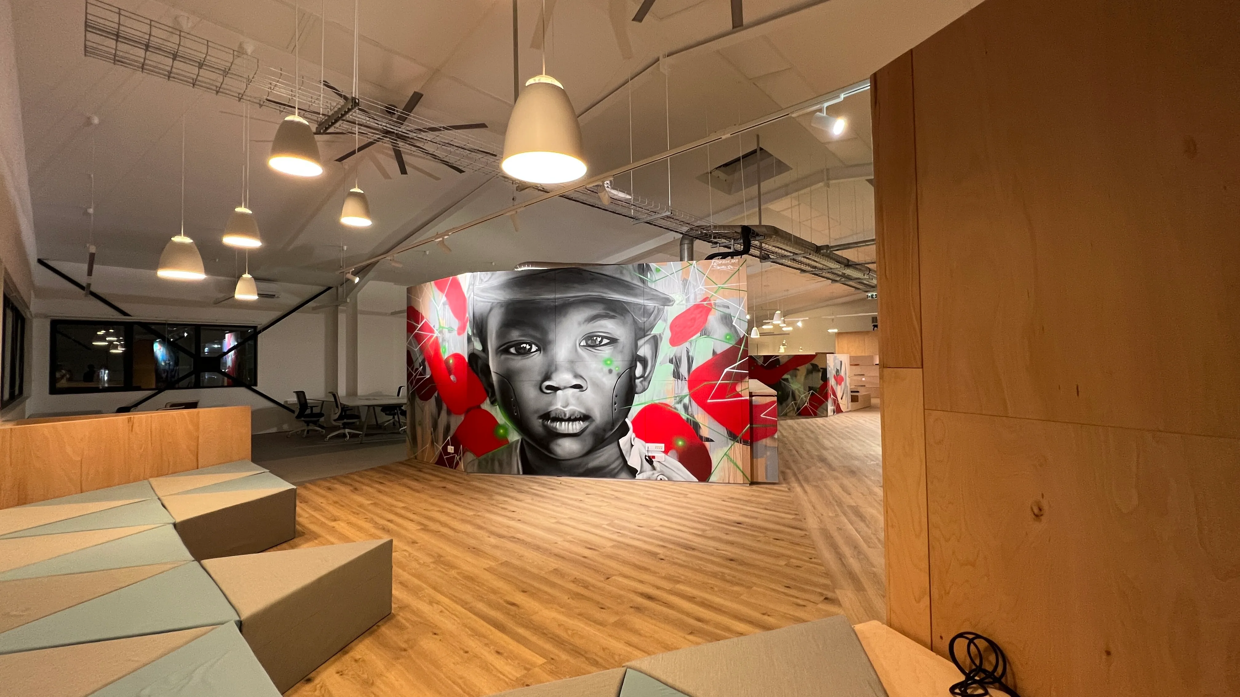Interior of Zebox Guadeloupe with a large mural of a boy's portrait on a freestanding partition, wooden flooring, pendant lights and angular lounge seating