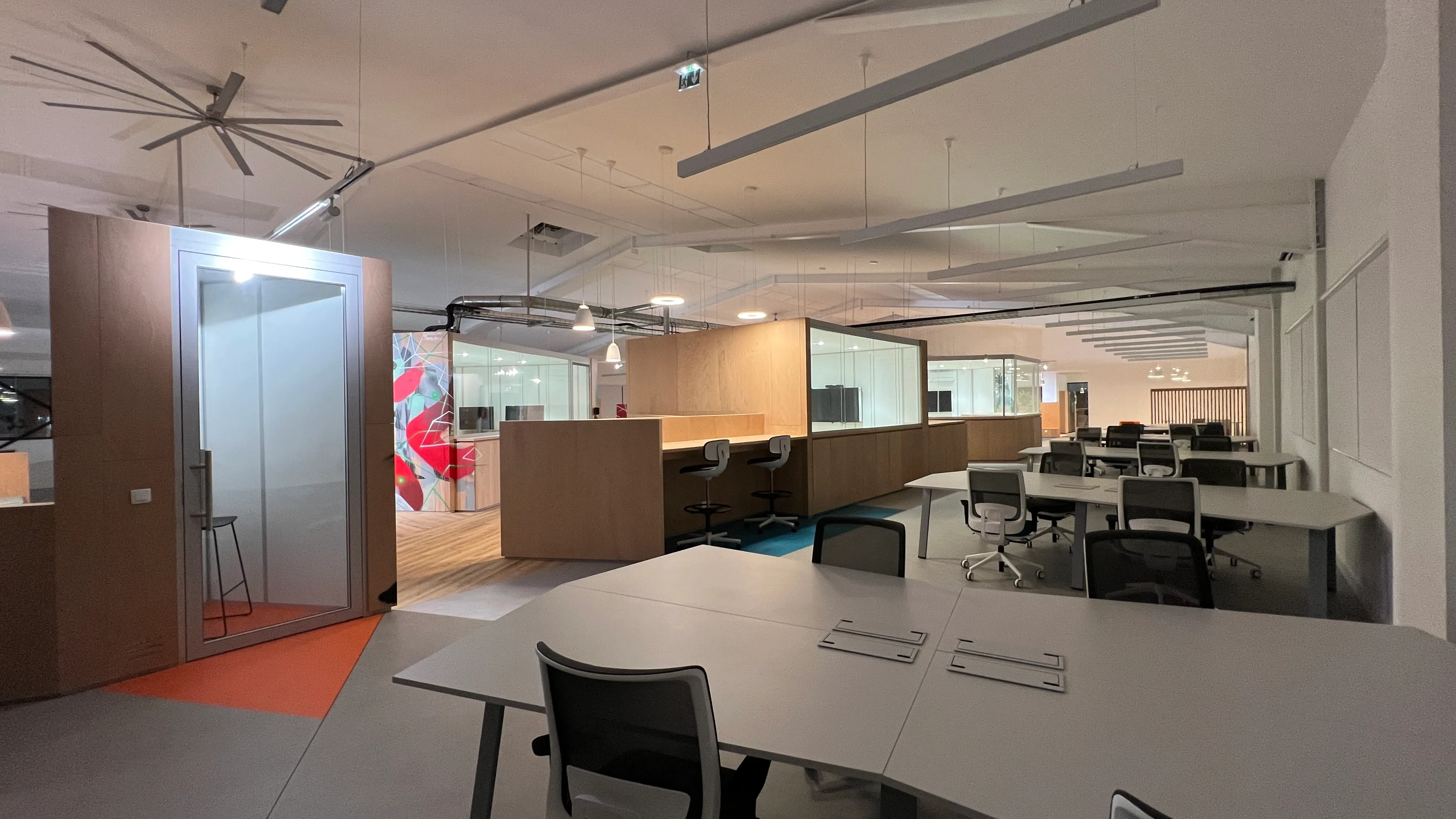 Open-plan office at Zebox Guadeloupe, wooden phone booth and meeting pods framing rows of workstations beneath exposed ceiling ductwork