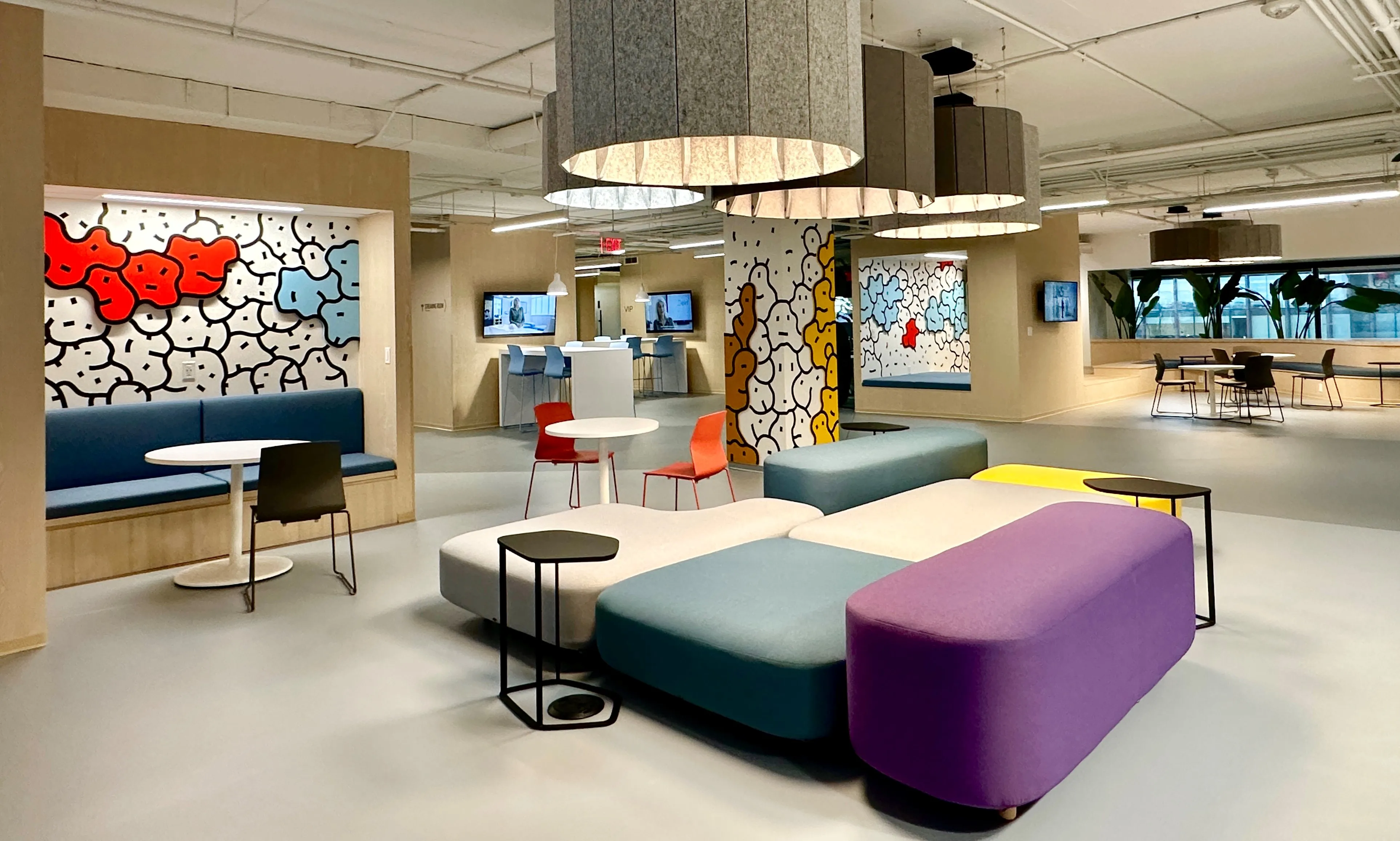 Lounge area in Zebox Washington with colourful modular seating, round tables and playful graphic wall murals under drum-shaped pendant lights