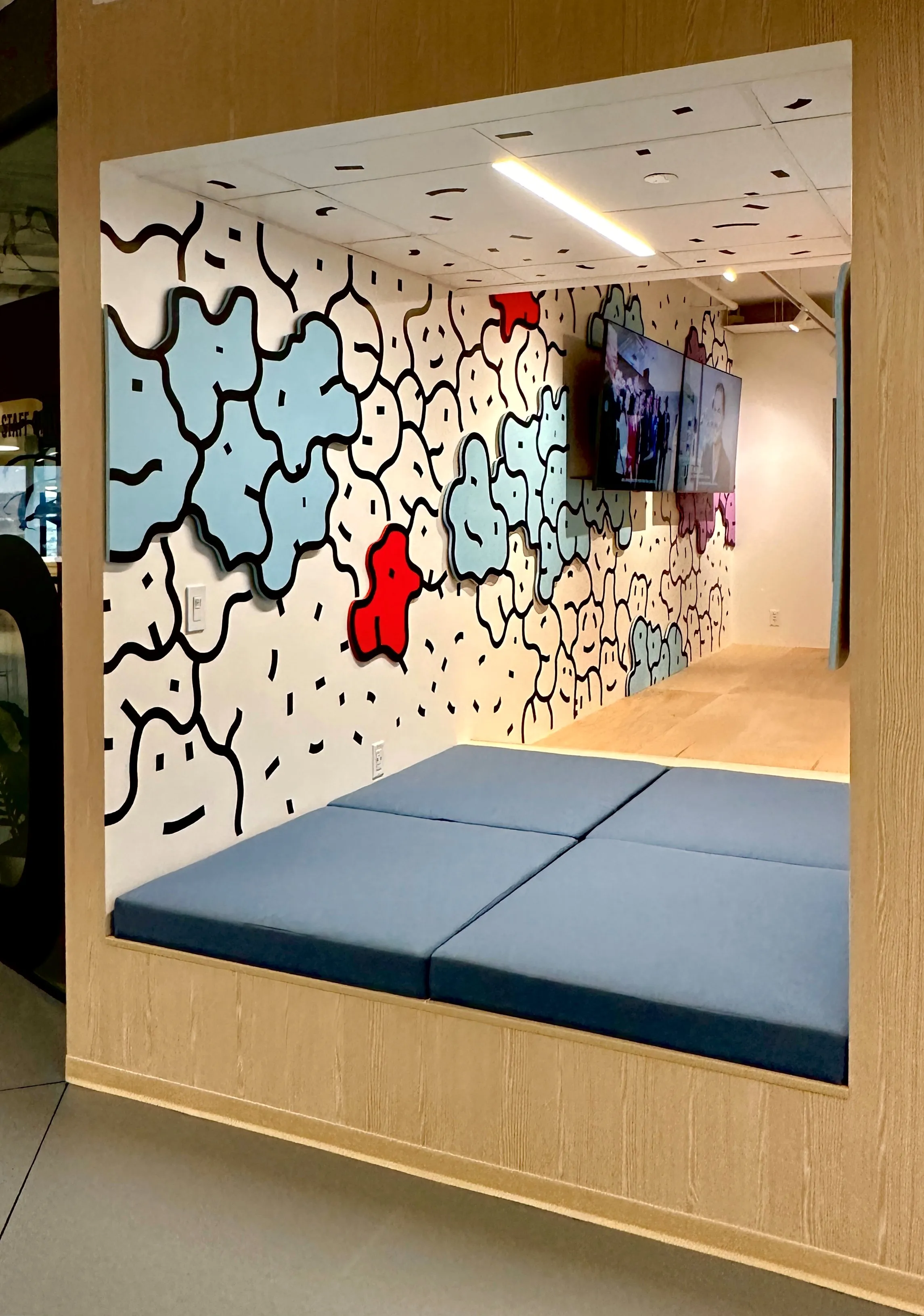 Nook seating alcove in Zebox Washington with blue cushioned bench beneath a wall mural of blue and red organic shapes outlined in black