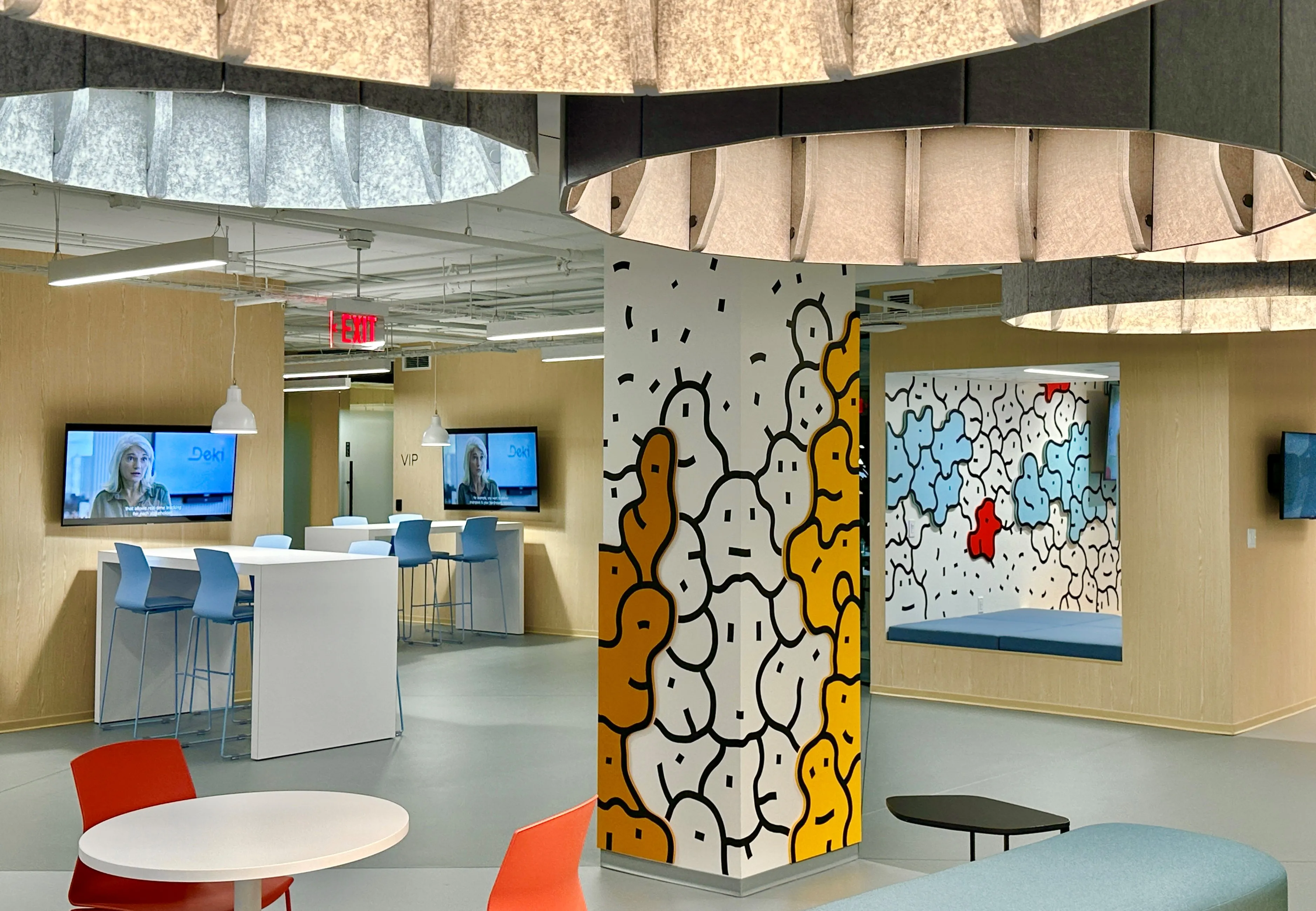 Breakout lounge in Zebox Washington with a cartoon-patterned column, oval acoustic ceiling panels, high tables with blue stools and screens displaying video calls