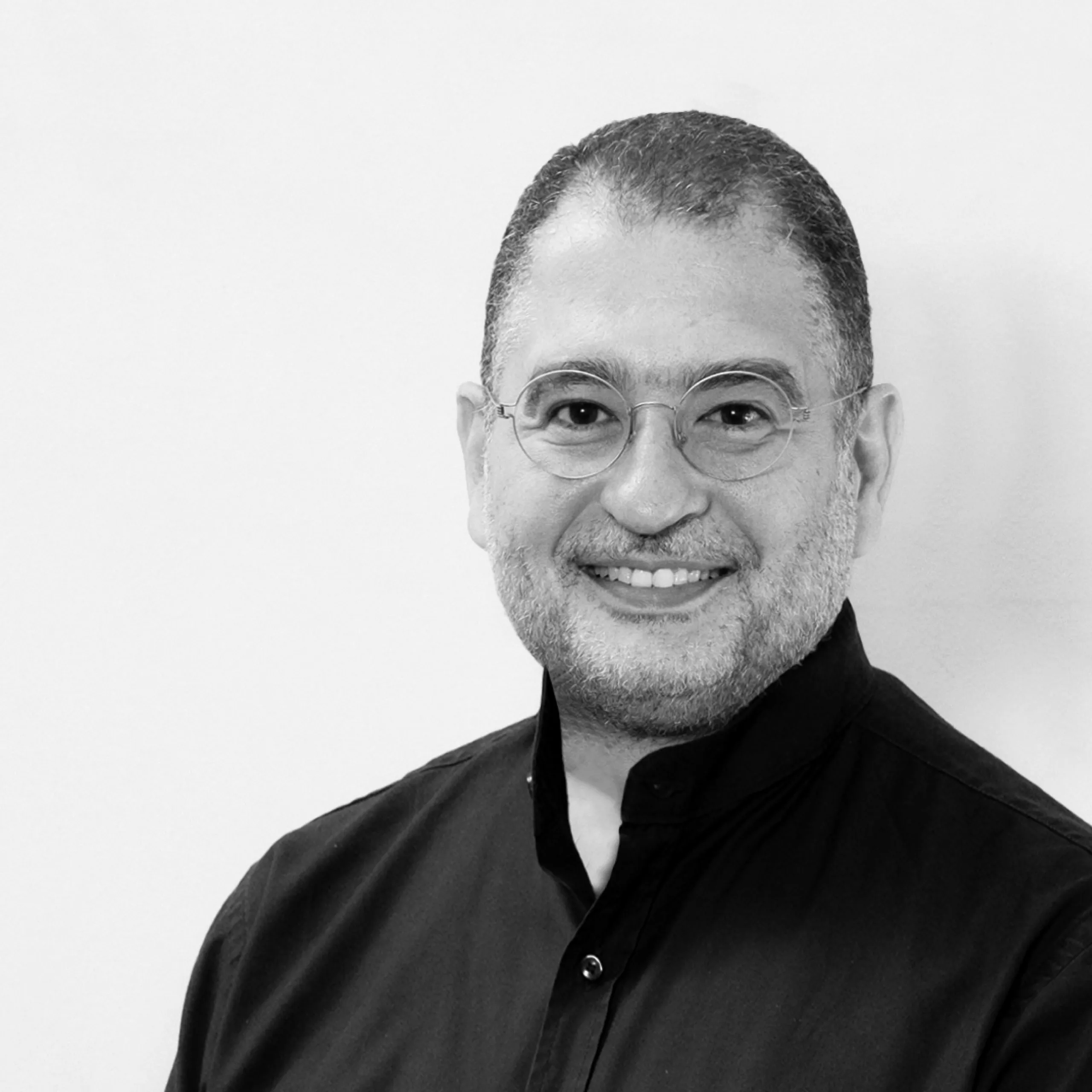 Youssef Nour, Senior Lead Architect at Nabil Gholam Architects, black and white portrait smiling in round glasses and a dark buttoned shirt