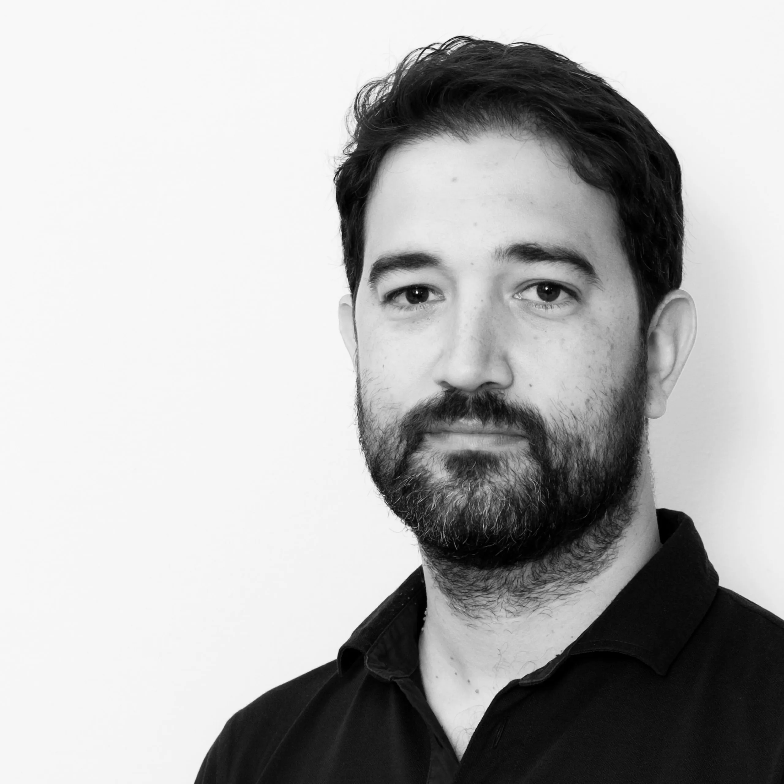 Hector Salcedo, Lead Architect at Nabil Gholam Architects, black and white portrait with a full beard wearing a dark collared shirt