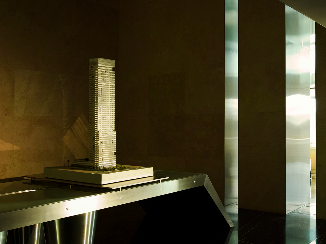 Illuminated scale model of Golden Tower's high-rise displayed on a metal table in the dim travertine-clad lobby in Jeddah