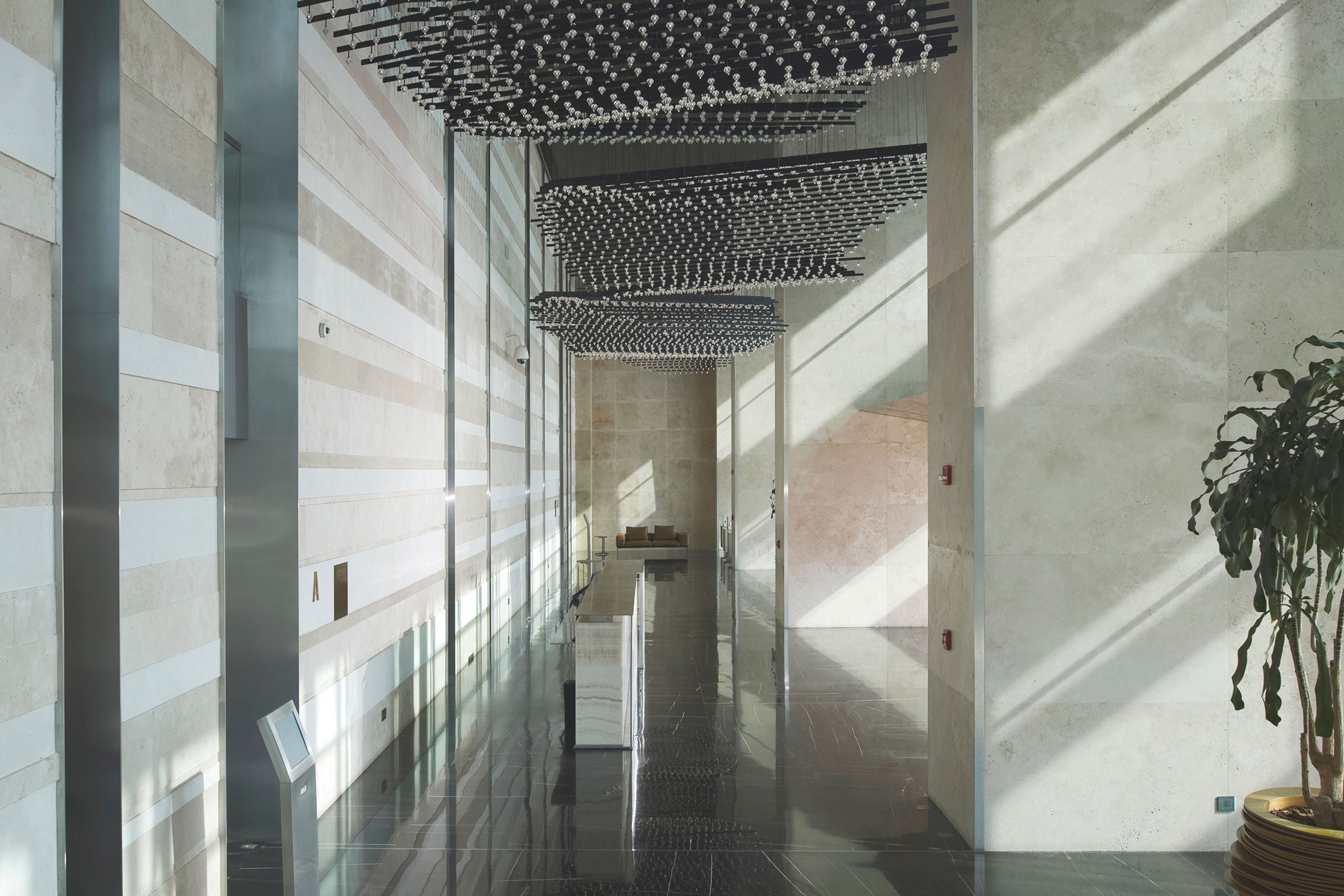 Lobby of Golden Tower's interior design in Jeddah, Saudi Arabia, striped travertine walls and suspended light installations catching sunlit reflections on dark marble floors