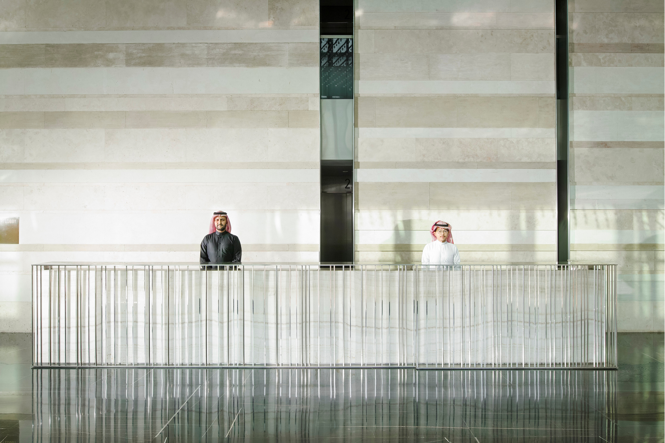 Reception lobby of Golden Tower in Jeddah, two attendants behind a slender vertical steel-baluster desk against a striped travertine wall