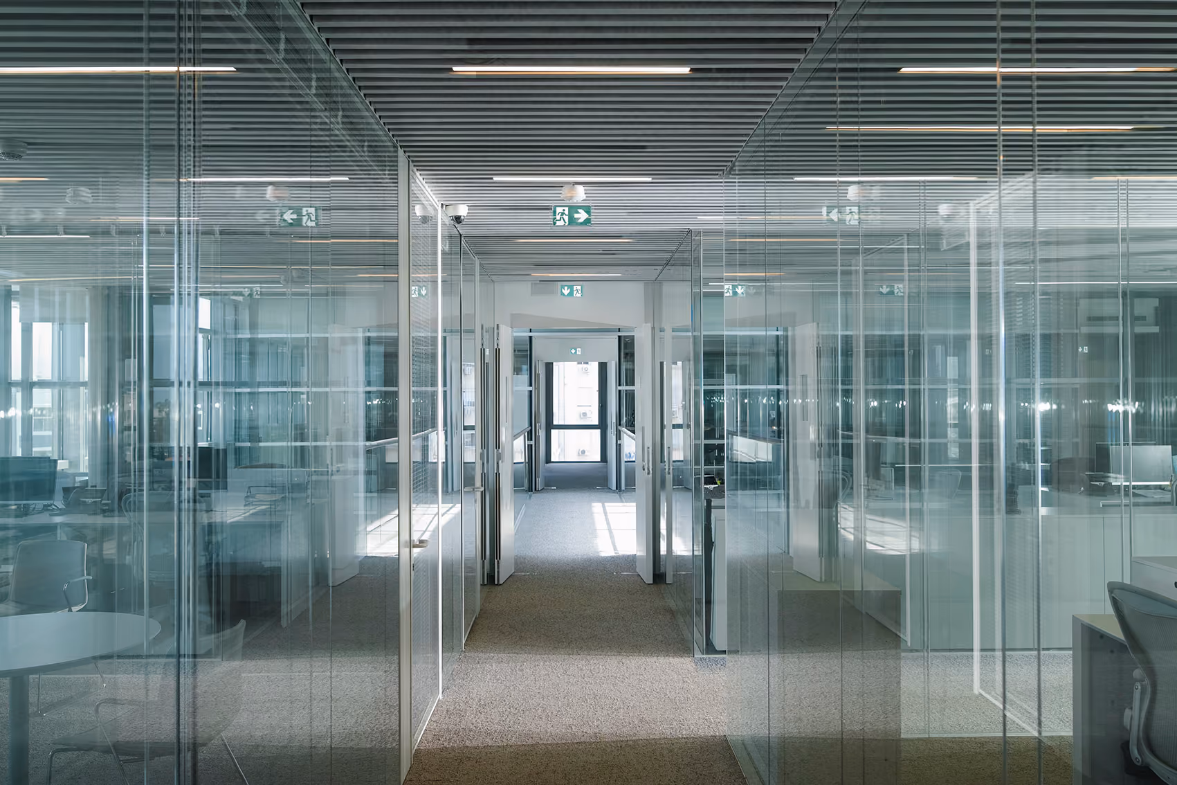 Glass-partitioned office corridor at CMA-CGM Headquarters in Beirut, ribbed ceiling and transparent walls lining a central walkway toward a bright window