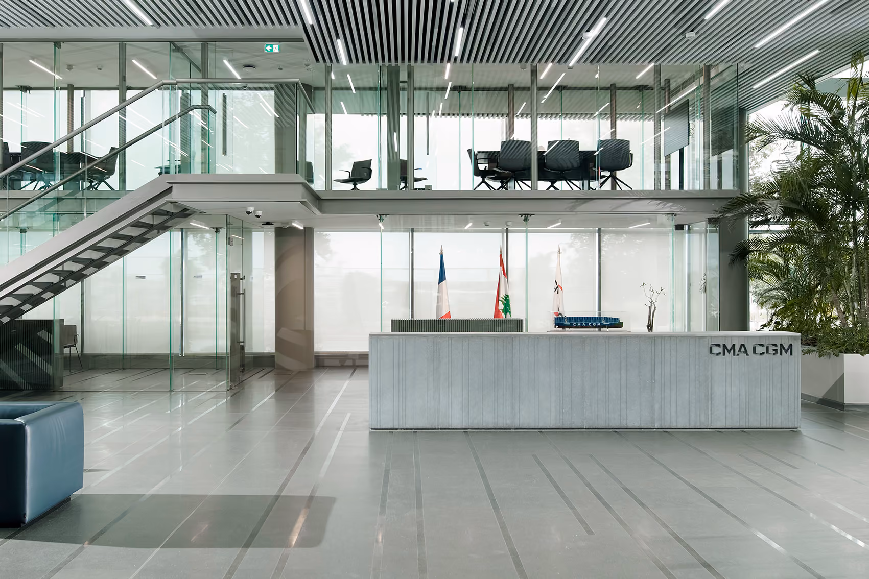 Reception lobby of CMA-CGM Headquarters in Beirut, a concrete-clad desk with the company logo beneath a glazed mezzanine bridge and staircase