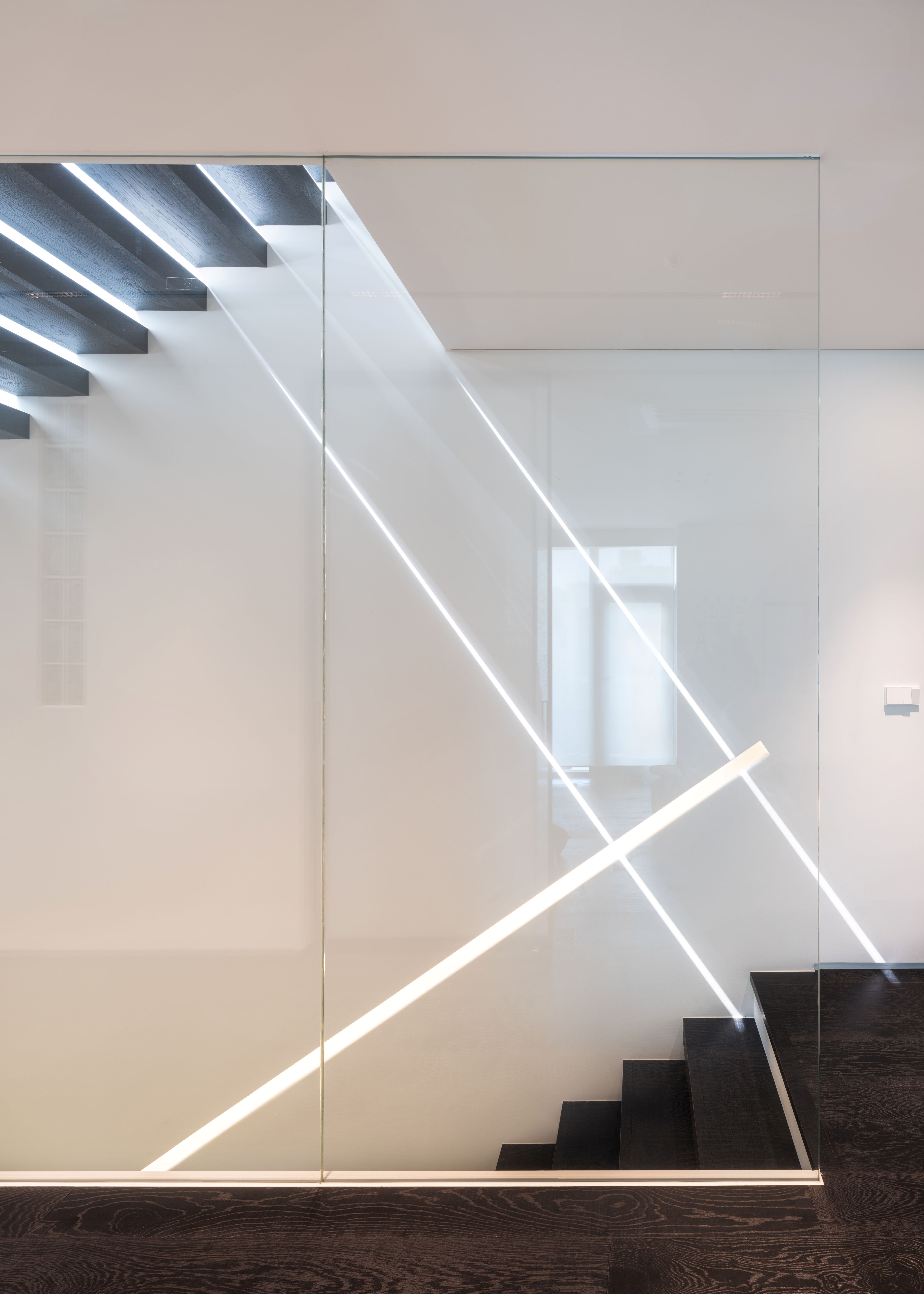Staircase in Pyrite, Seoul, dark timber treads under a glass balustrade with diagonal LED light strips casting bright lines across a white wall