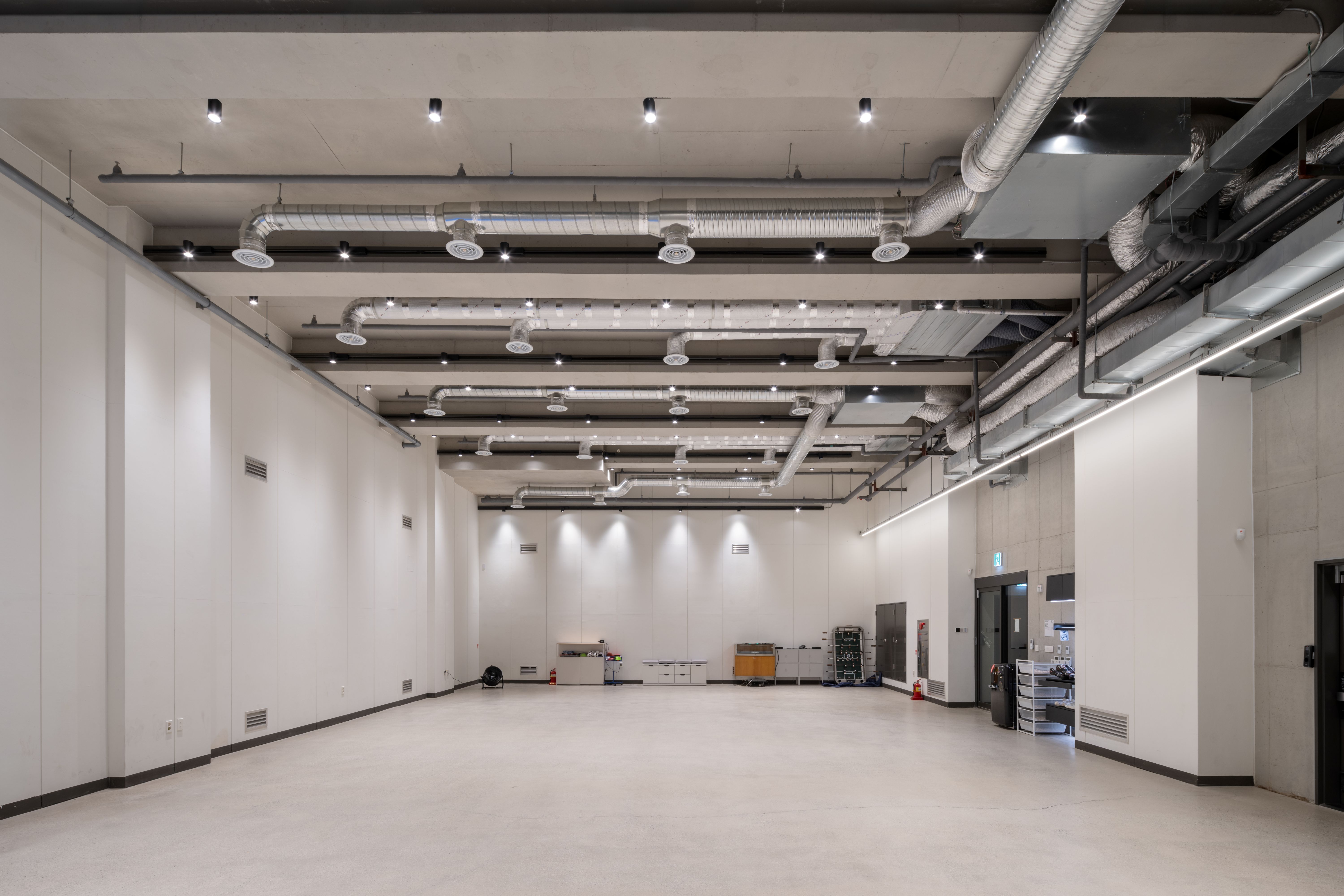 Empty industrial-style space in Pyrite, Seoul, with exposed ductwork and lighting tracks over white walls and bare concrete floor