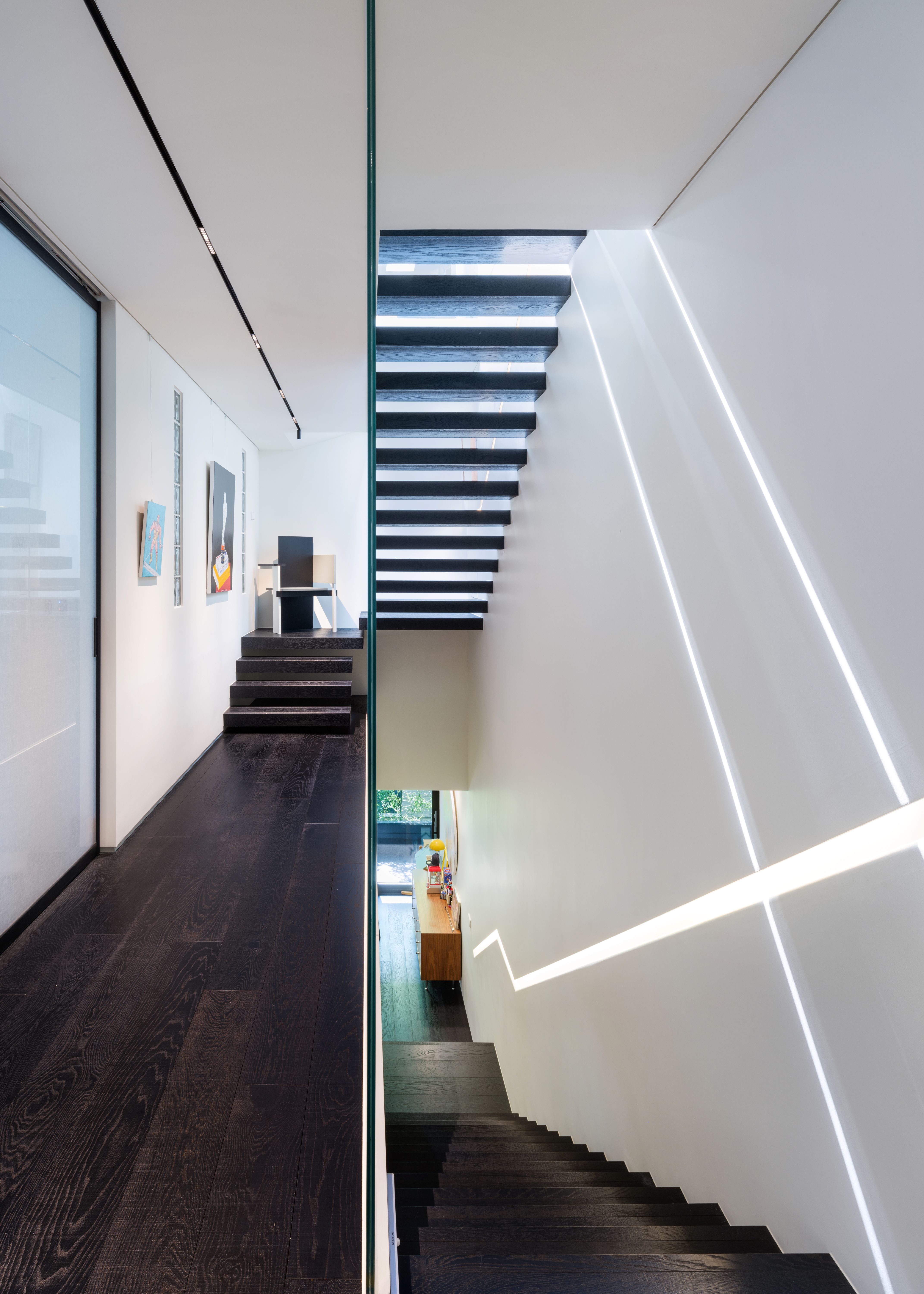 Floating dark timber staircase in Pyrite, Seoul, lit by angled linear skylights against a white stairwell wall