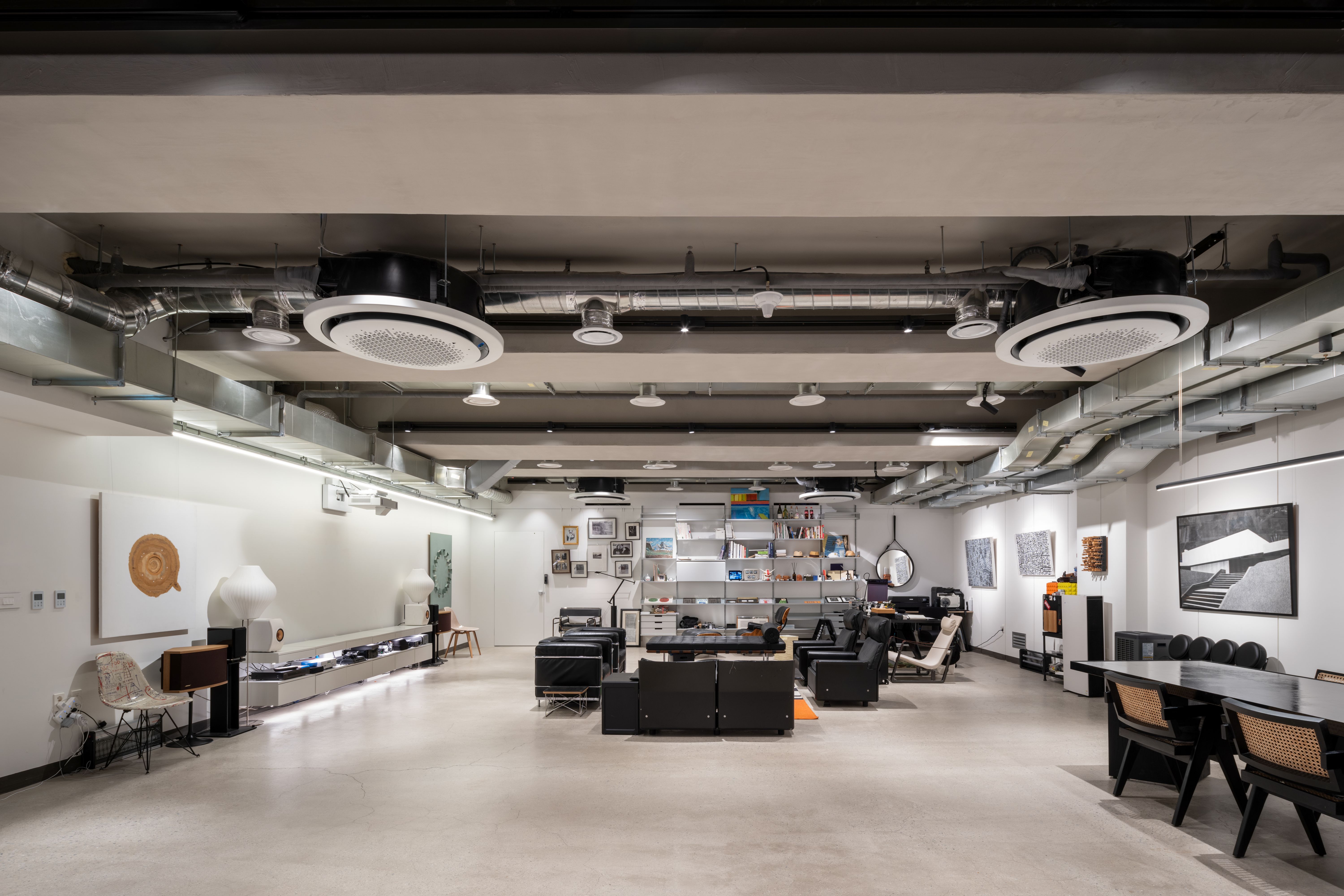 Open-plan lounge in Pyrite, Seoul, with exposed ceiling ductwork, black leather seating, shelving and artwork along the walls