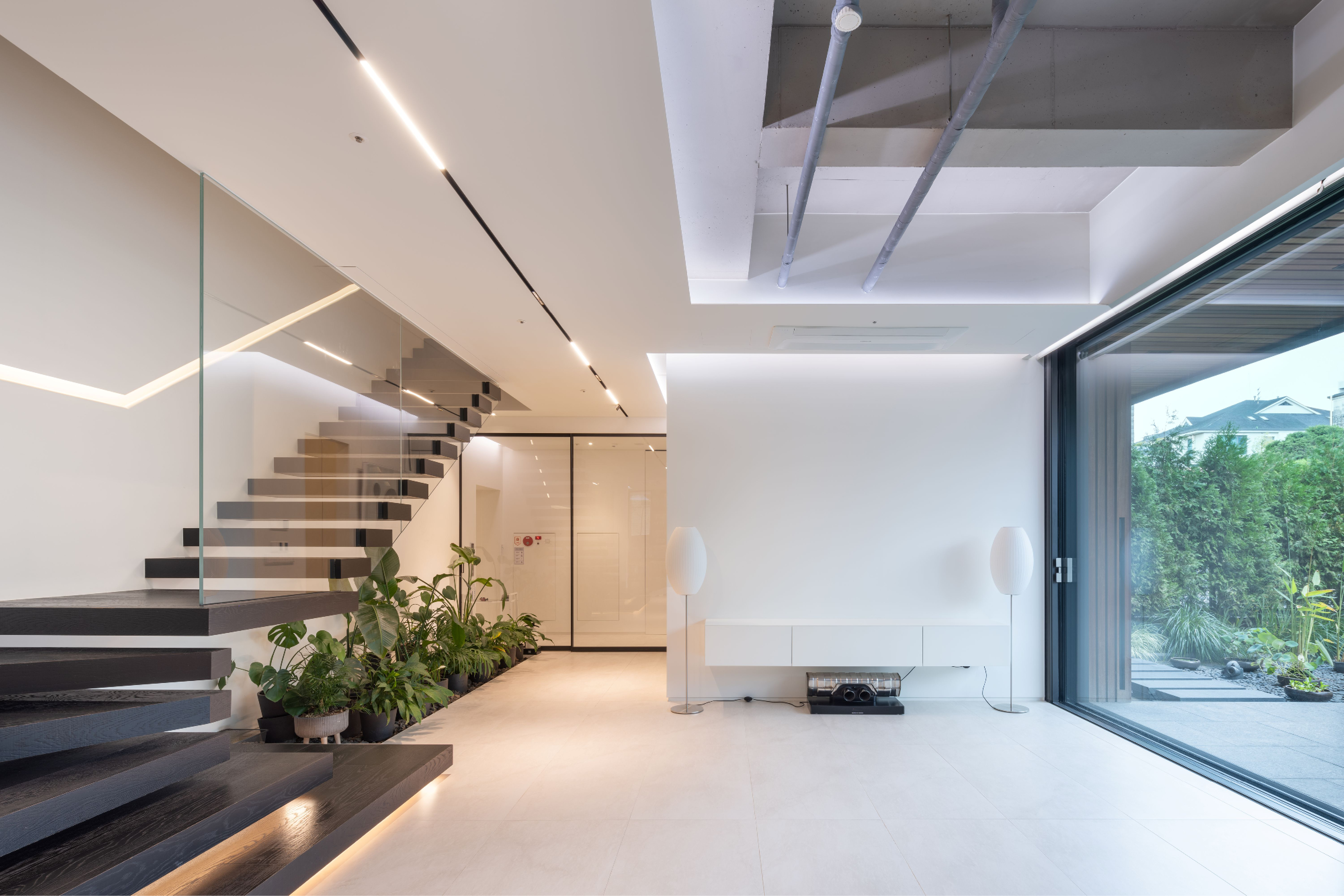 Pyrite, a private residence interior by Nabil Gholam Architects in Seoul, floating dark timber stair with glass balustrade beside planters and a glazed garden view
