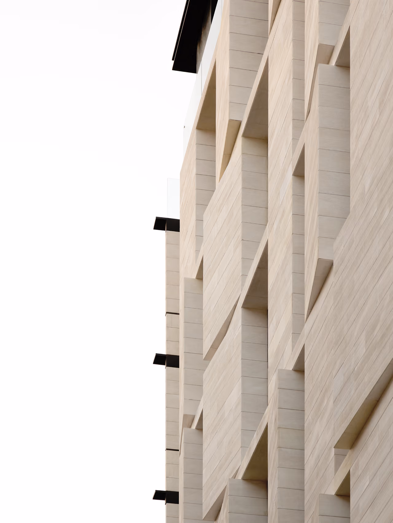 Close-up facade detail of Allenby Gate in Beirut, angled stone fins casting deep shadows in a rhythmic diagonal pattern against a pale sky
