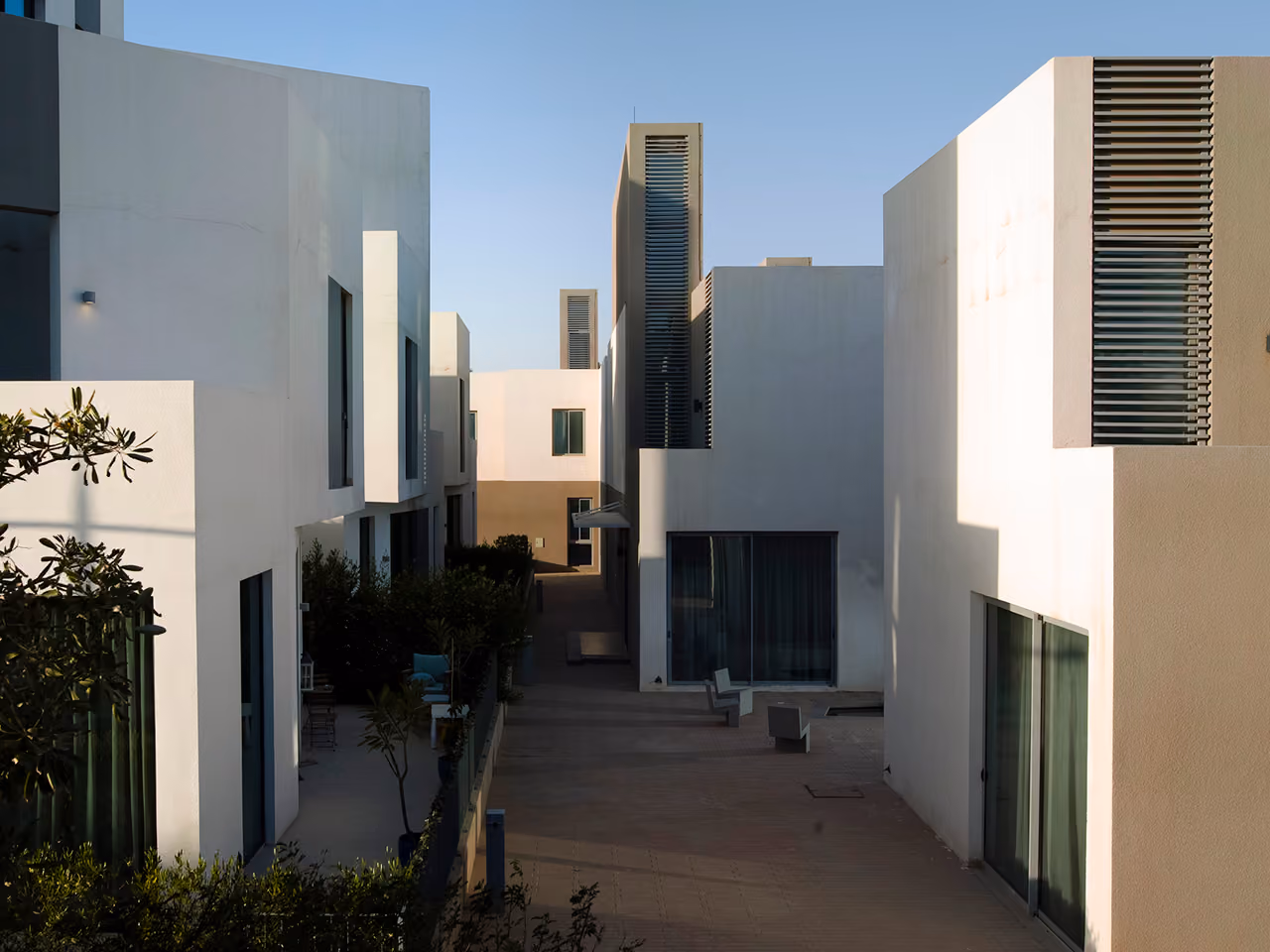 Courtyard passage between white villas at Qortuba Oasis in Riyadh, cubic massing with slatted ventilation towers and glazed terraces