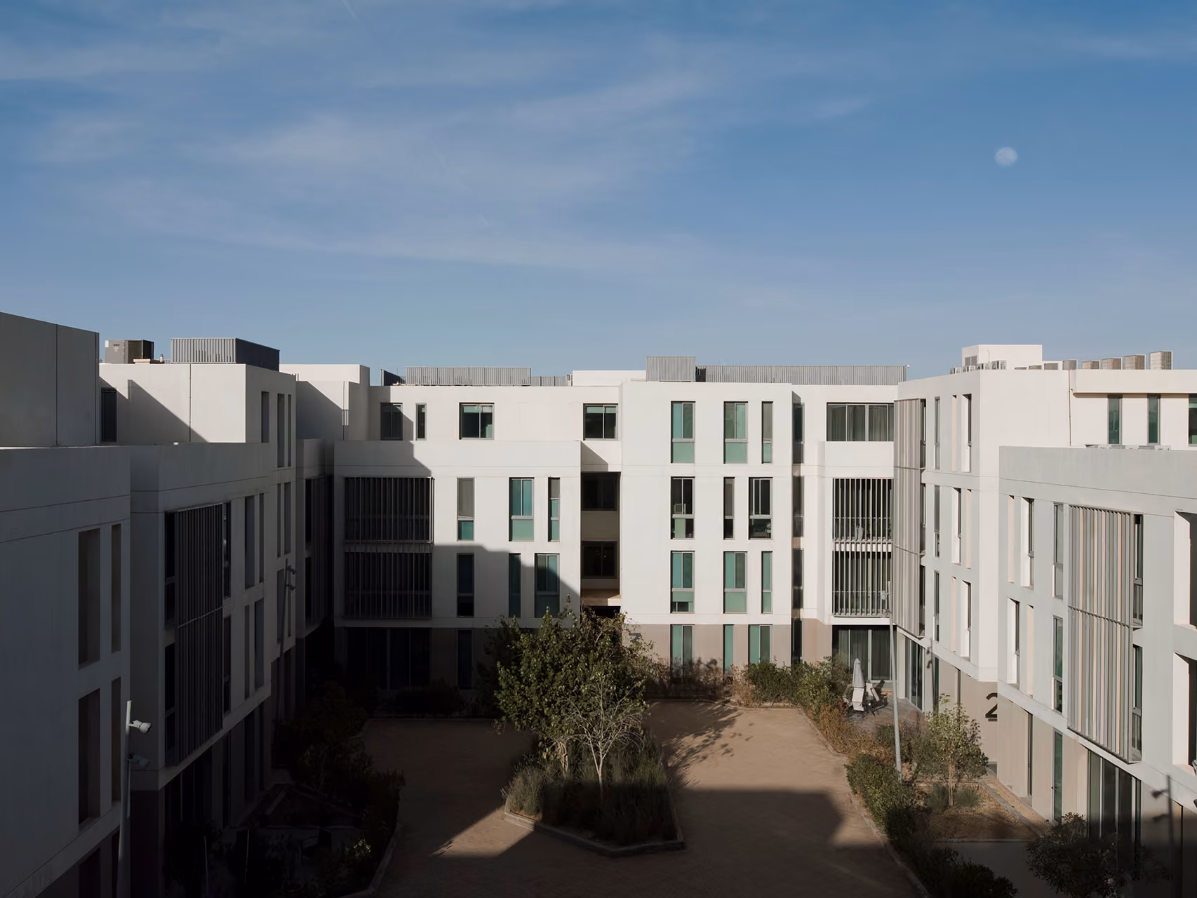 Interior courtyard of Qortuba Oasis in Riyadh, low-rise apartment blocks with green-tinted windows and louvred balconies around a landscaped garden