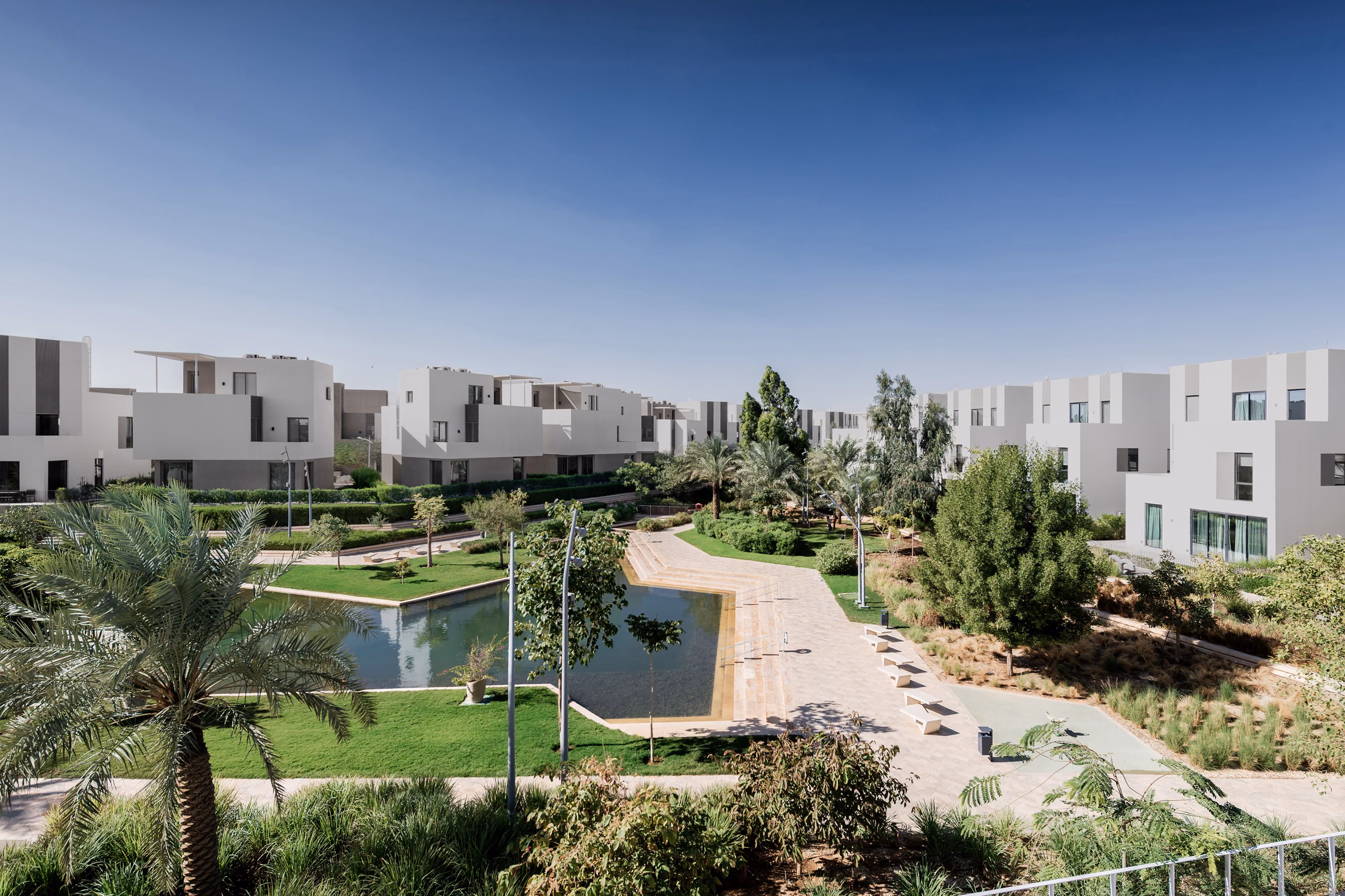 Qortuba Oasis, a low-rise residential compound by Nabil Gholam Architects, with white villas overlooking a landscaped garden and reflecting pool in Riyadh, Saudi Arabia