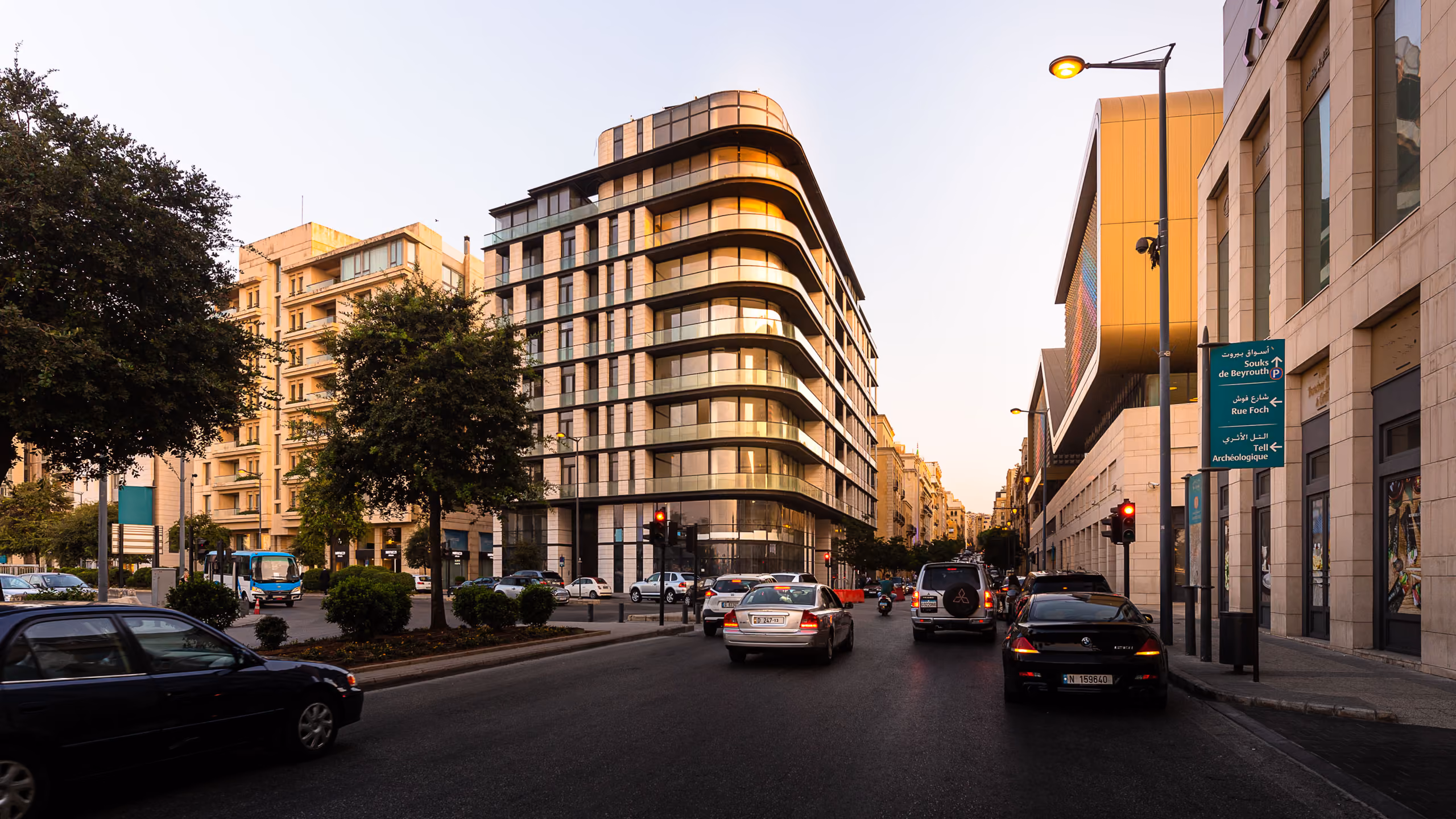 Allenby Gate, a curved corner residential building by Nabil Gholam Architects with rounded balconies, at a busy street intersection in downtown Beirut, Lebanon, at dusk