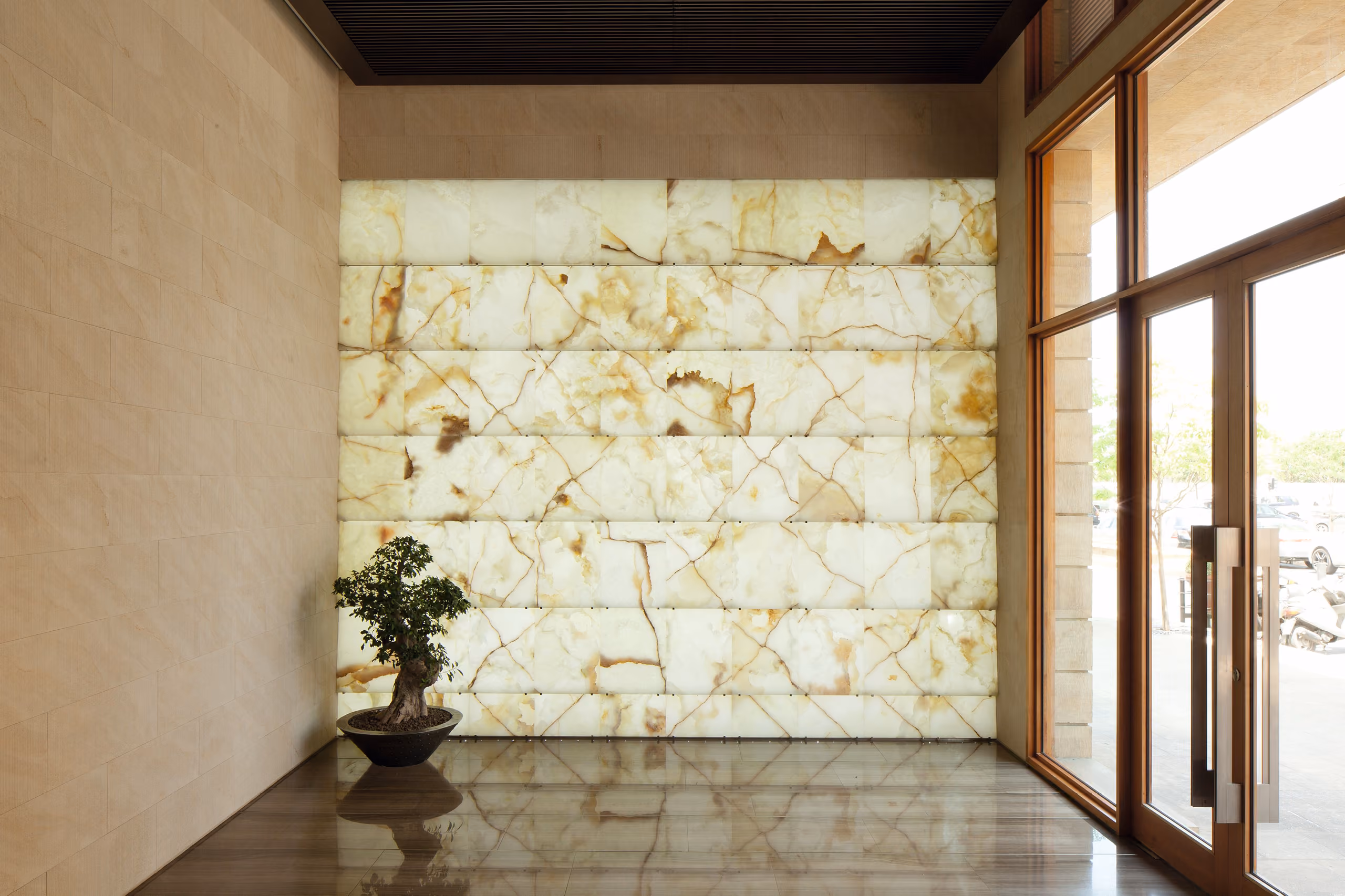 Lobby of the Waqf Foch Office Building in Beirut, backlit onyx wall with amber veining, a bonsai tree and glazed timber entrance doors