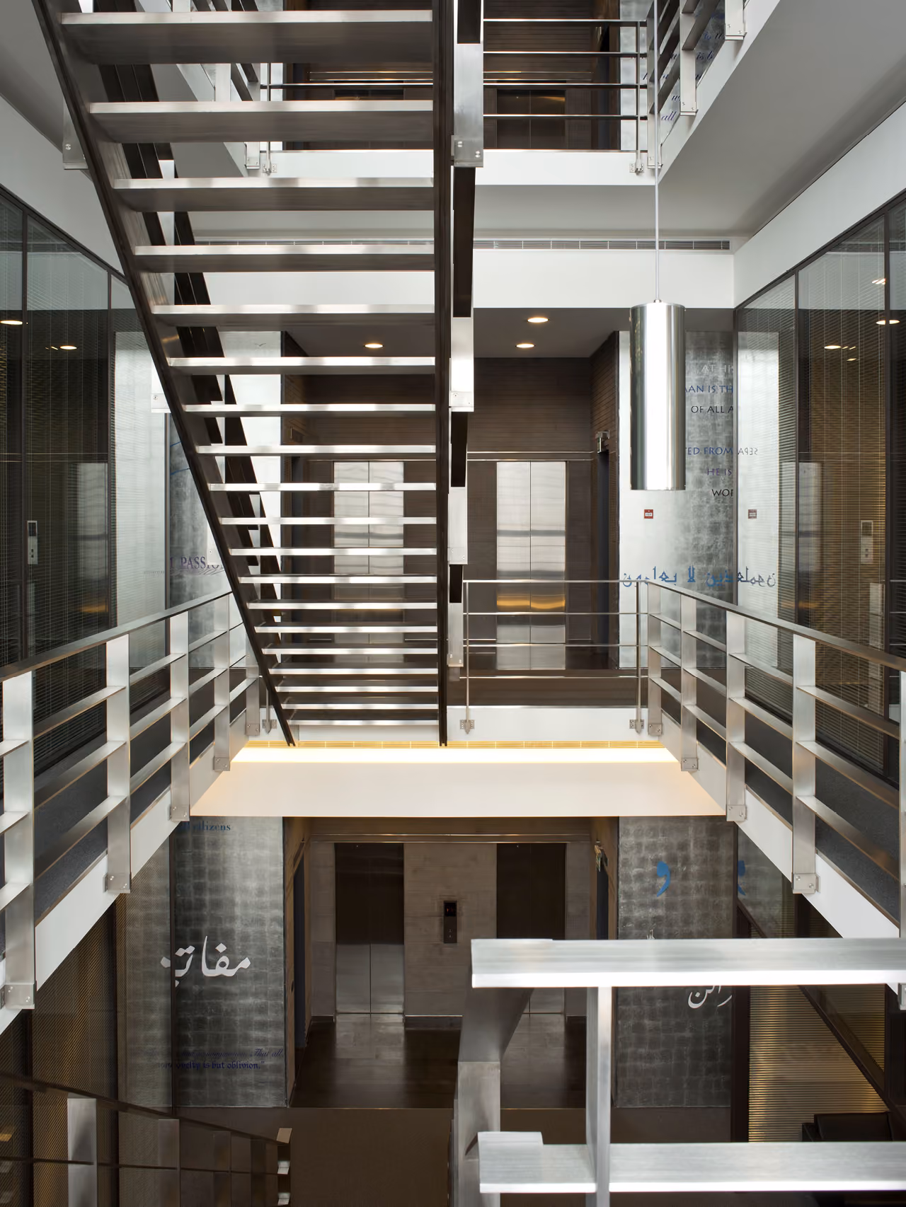 Interior atrium of Waqf Foch Office Building in Beirut, metal staircase and glass-railed landings around a central void with Arabic and English wall text