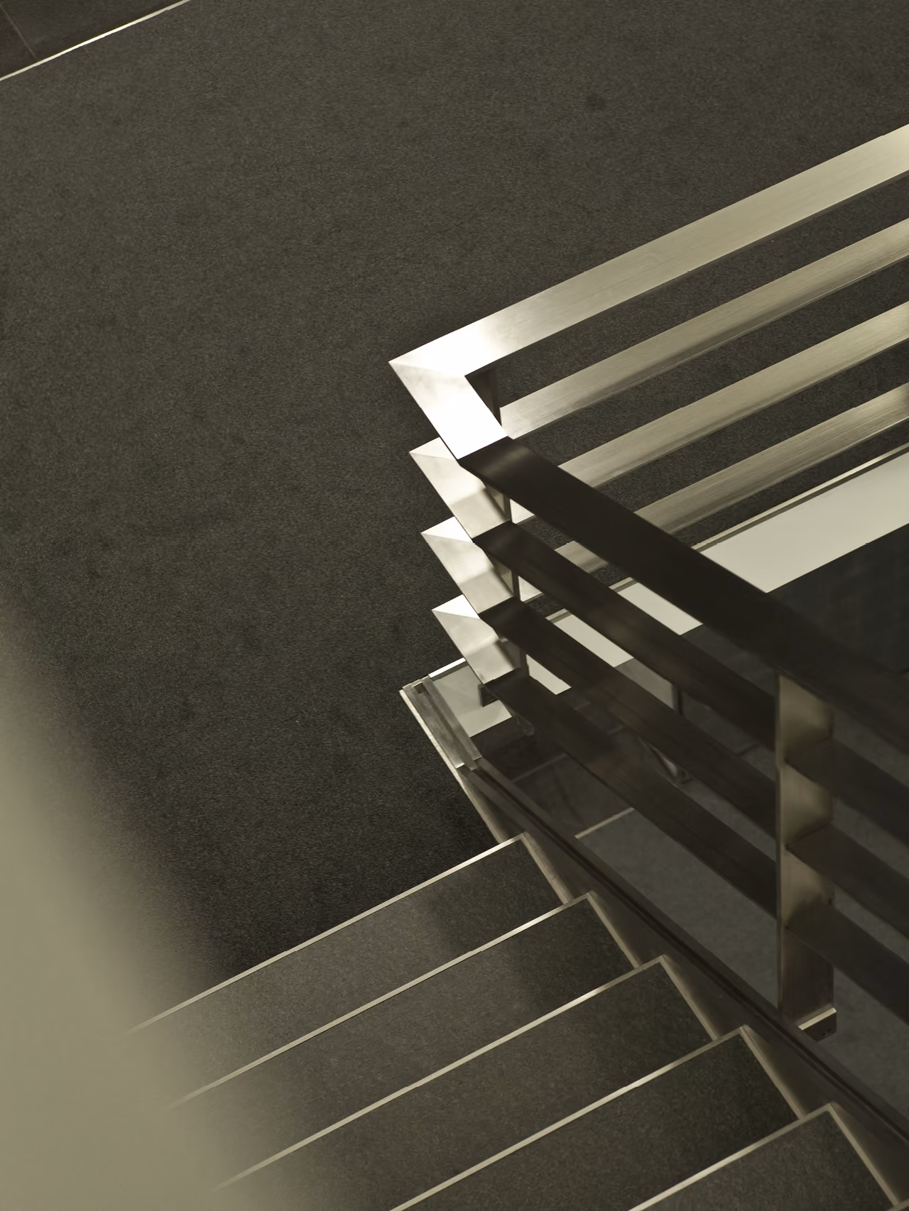 Staircase detail in the Waqf Foch Office Building interior in Beirut, brushed steel horizontal railings angled above dark stone treads