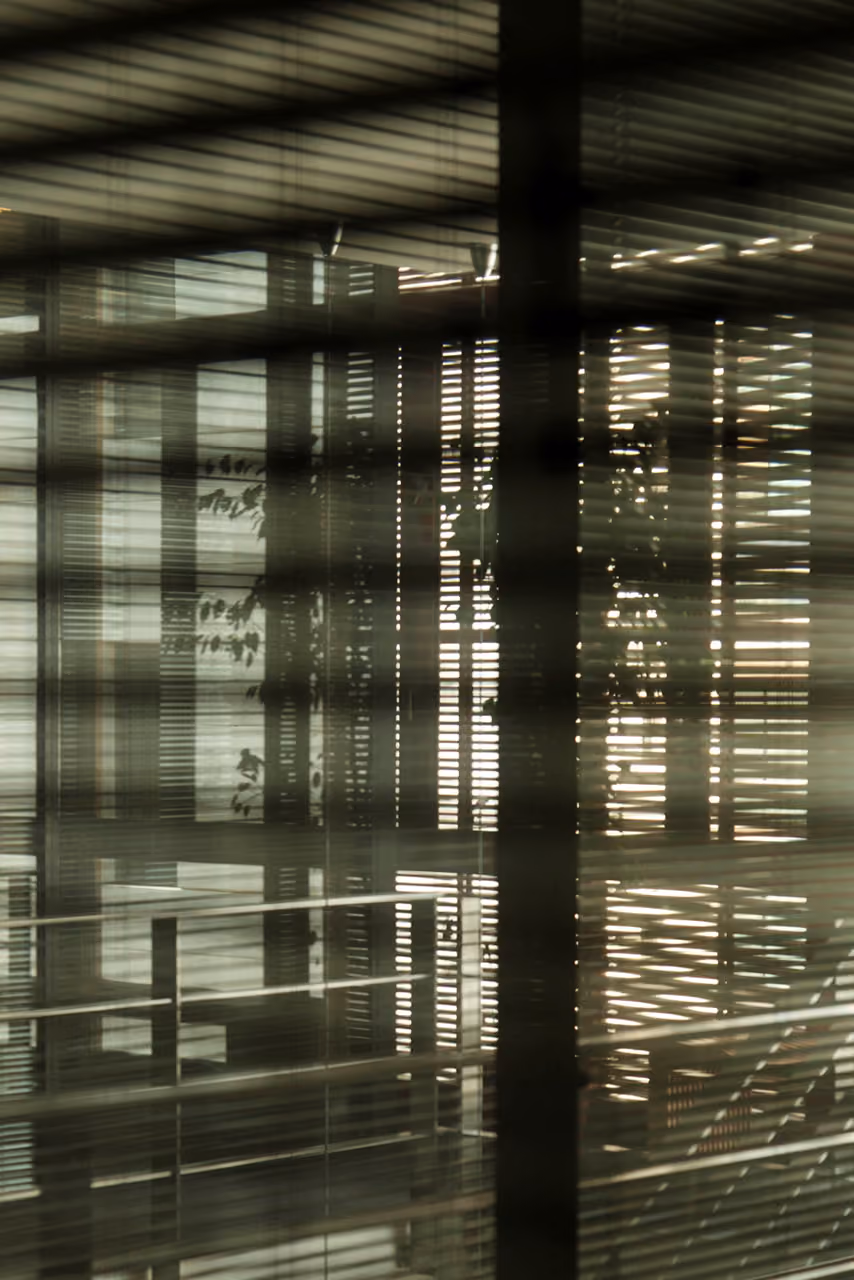 Layered horizontal blinds inside the Waqf Foch Office Building in Beirut, casting striped shadows and light across glass partitions and reflective surfaces