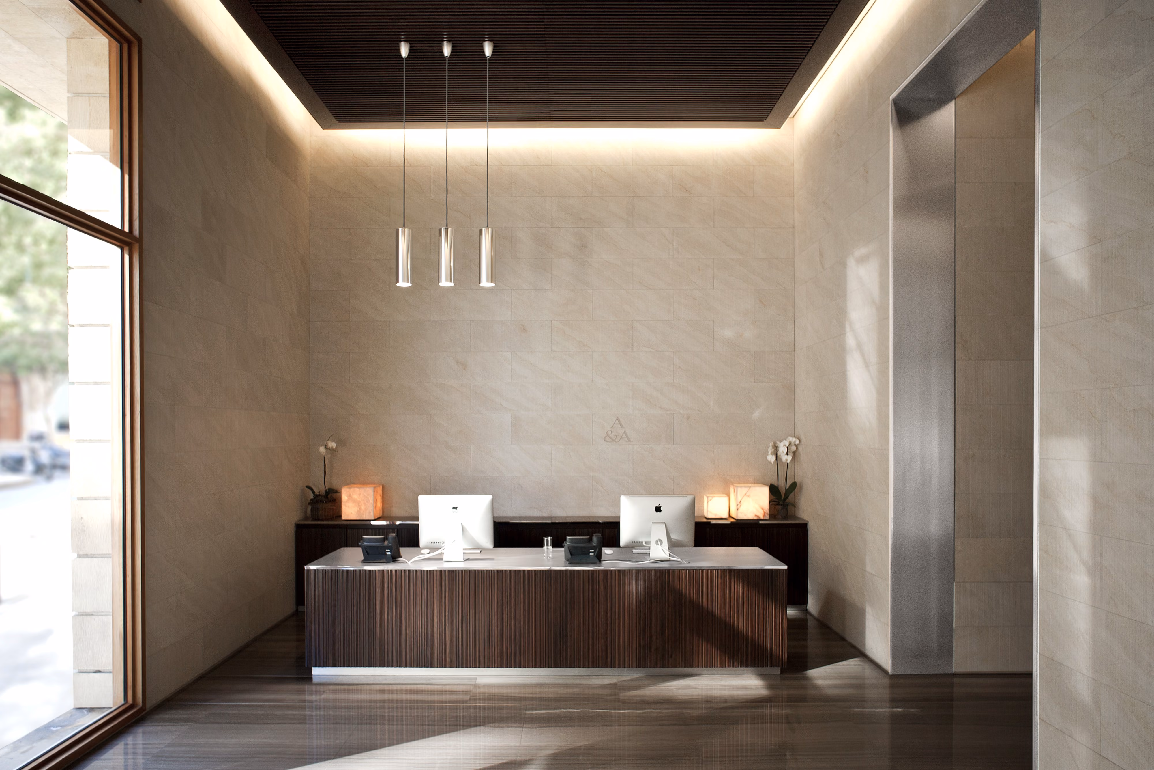 Reception lobby of the Waqf Foch Office Building in Beirut, Lebanon, by Nabil Gholam Architects, with a dark wood desk beneath pendant lights against stone-clad walls