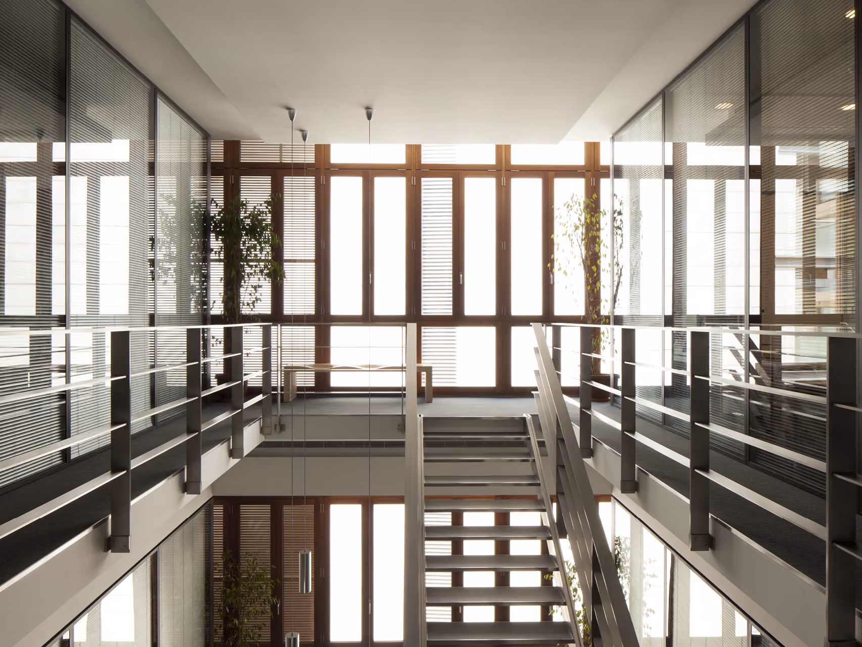 Interior atrium of the Waqf Foch Office Building in Beirut, glass-walled offices flanking a steel staircase beneath tall timber-framed windows and potted plants