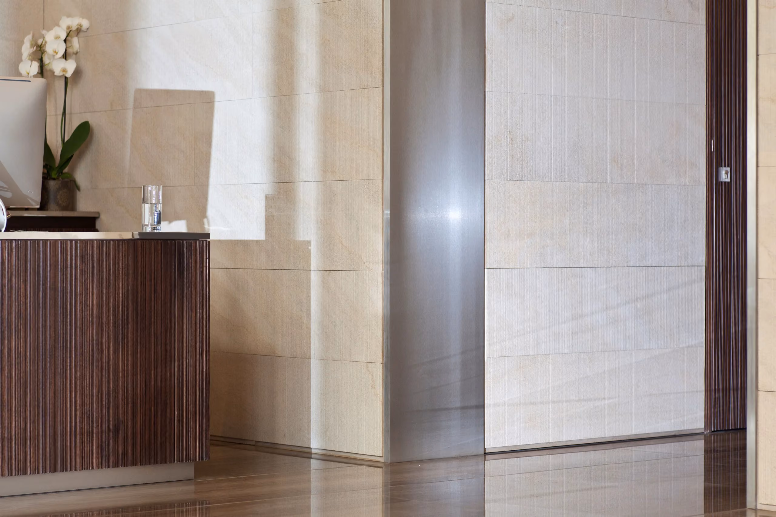 Reception area of the Waqf Foch Office Building interior in Beirut, dark wood-veneer desk with orchids beside stone-clad walls and a brushed steel column