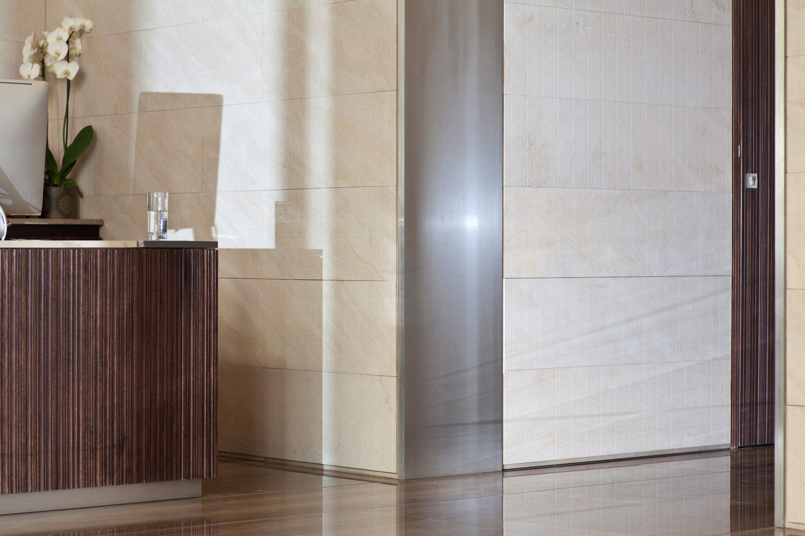 Reception area of the Waqf Foch Office Building interior in Beirut, dark wood-veneer desk with orchids beside stone-clad walls and a brushed steel column