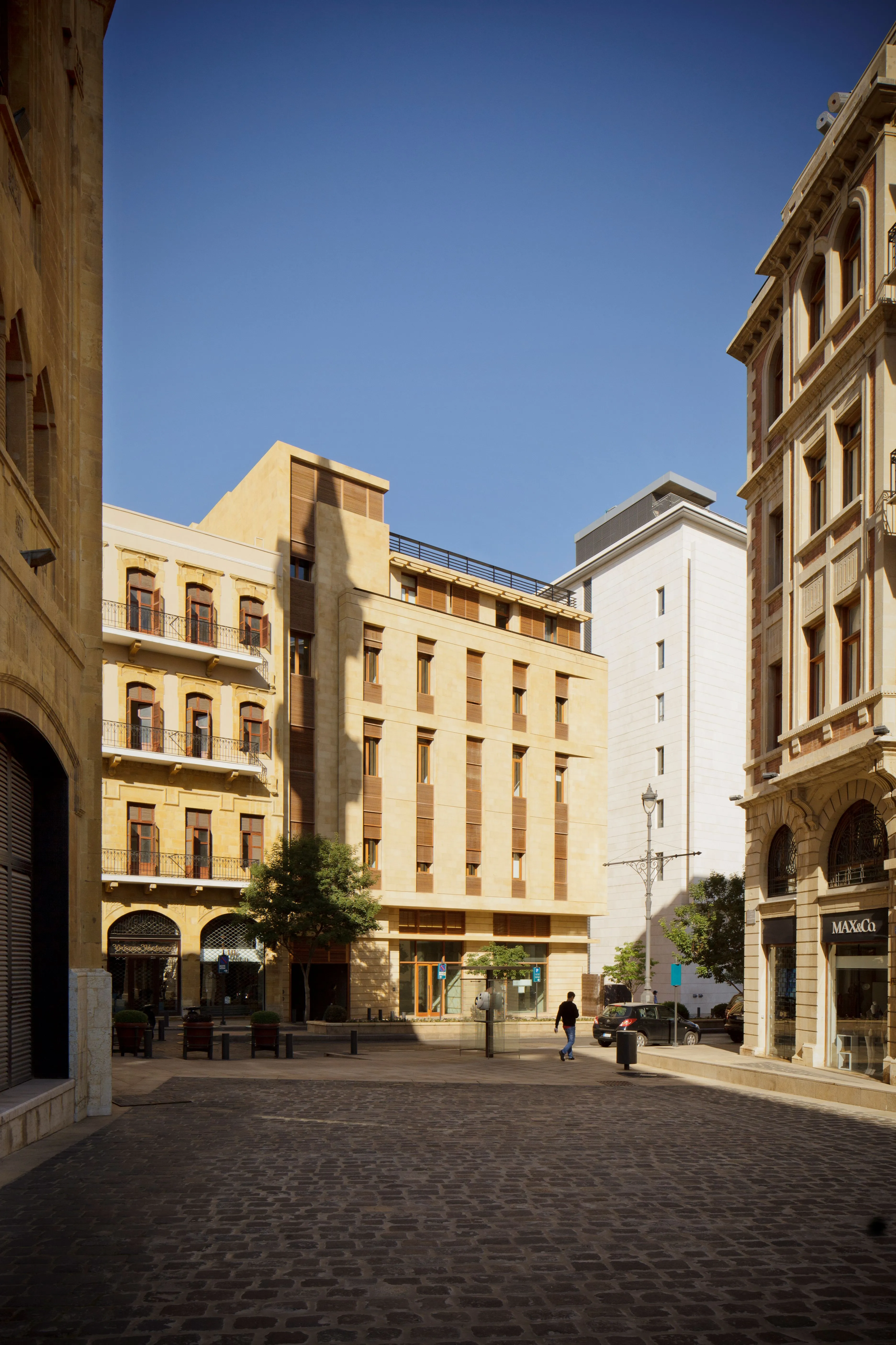 Waqf Foch Office Building in Beirut, sandstone-clad facade rising above cobblestone street, flanked by heritage arcaded buildings in the city centre
