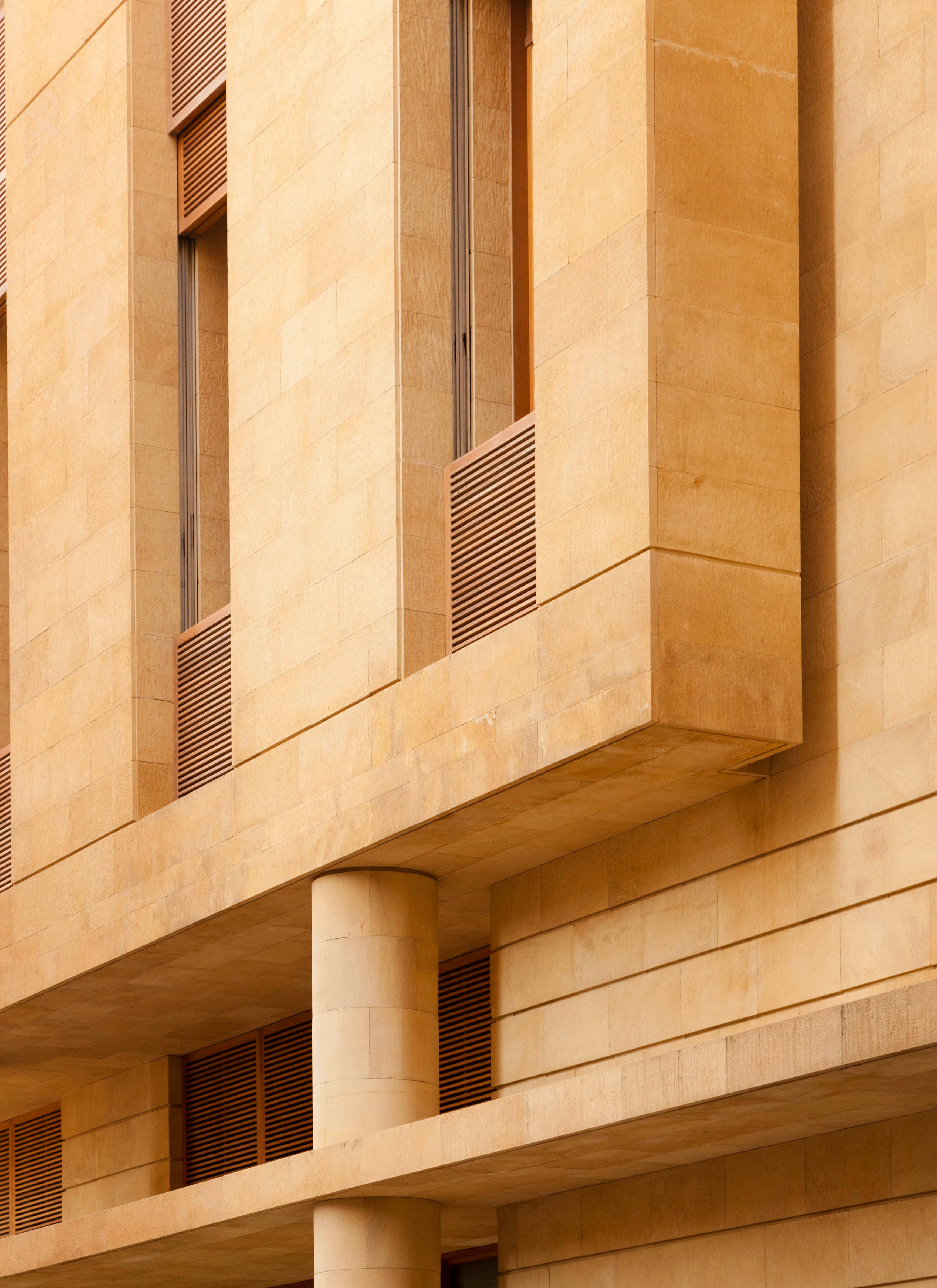 Facade detail of Waqf Foch Office Building in Beirut, sandstone cladding with cantilevered corners, louvred shutters and a cylindrical column
