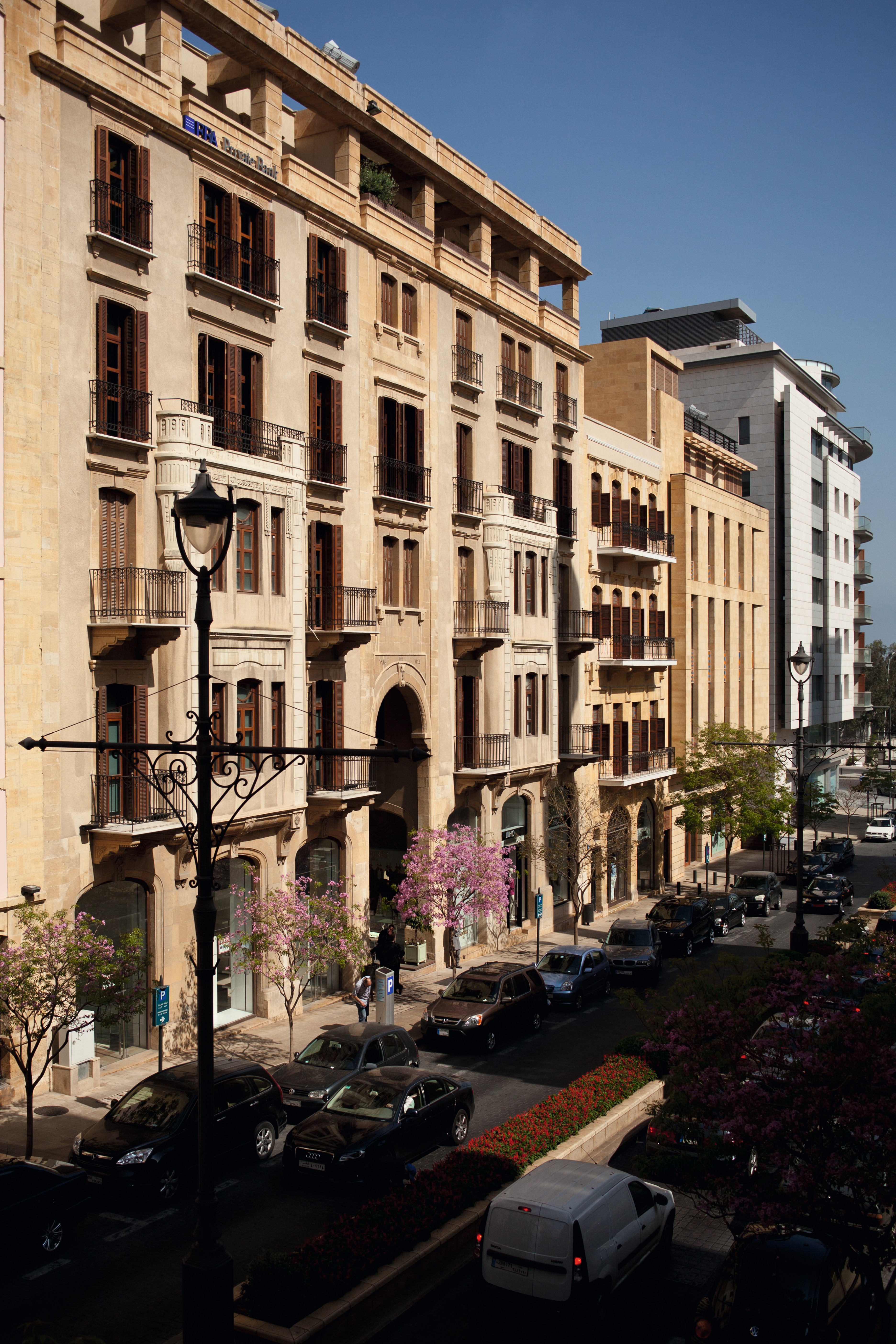Waqf Foch Office Building in Beirut, sandstone facade with shuttered windows and balconies along a tree-lined street with parked cars